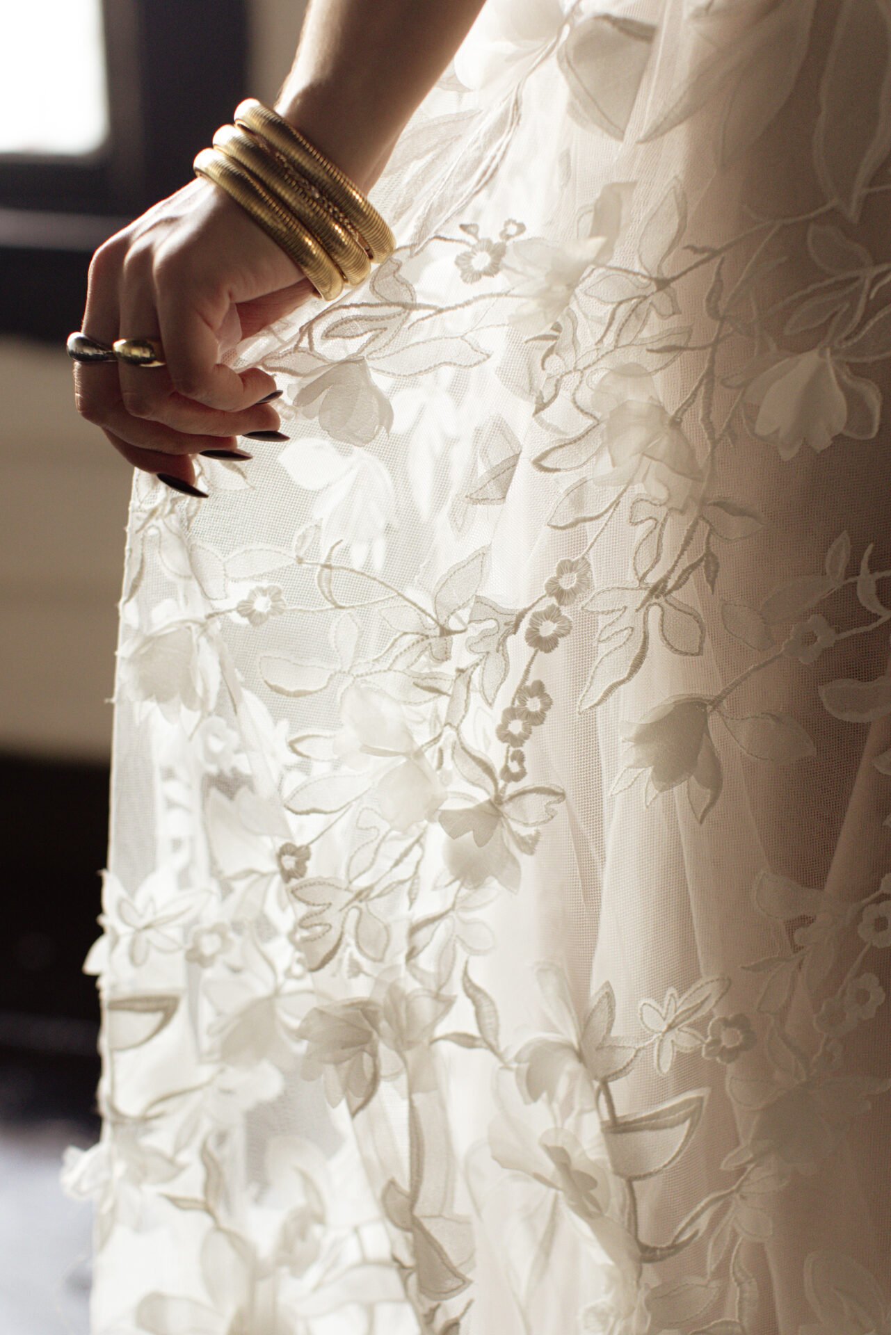 Close-up of a woman's hand resting on a white, floral lace fabric, with gold bangles on her wrist.