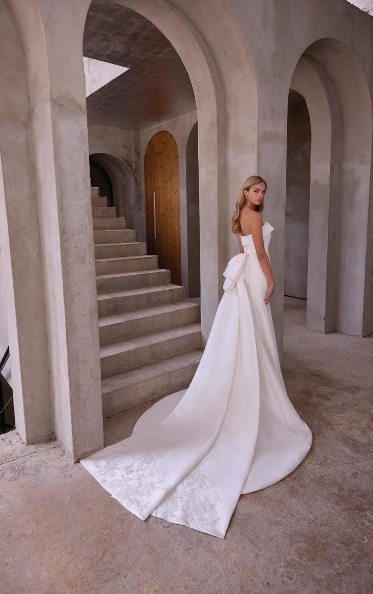 A woman in a white wedding gown standing inside a modern concrete building with arches and stairs.