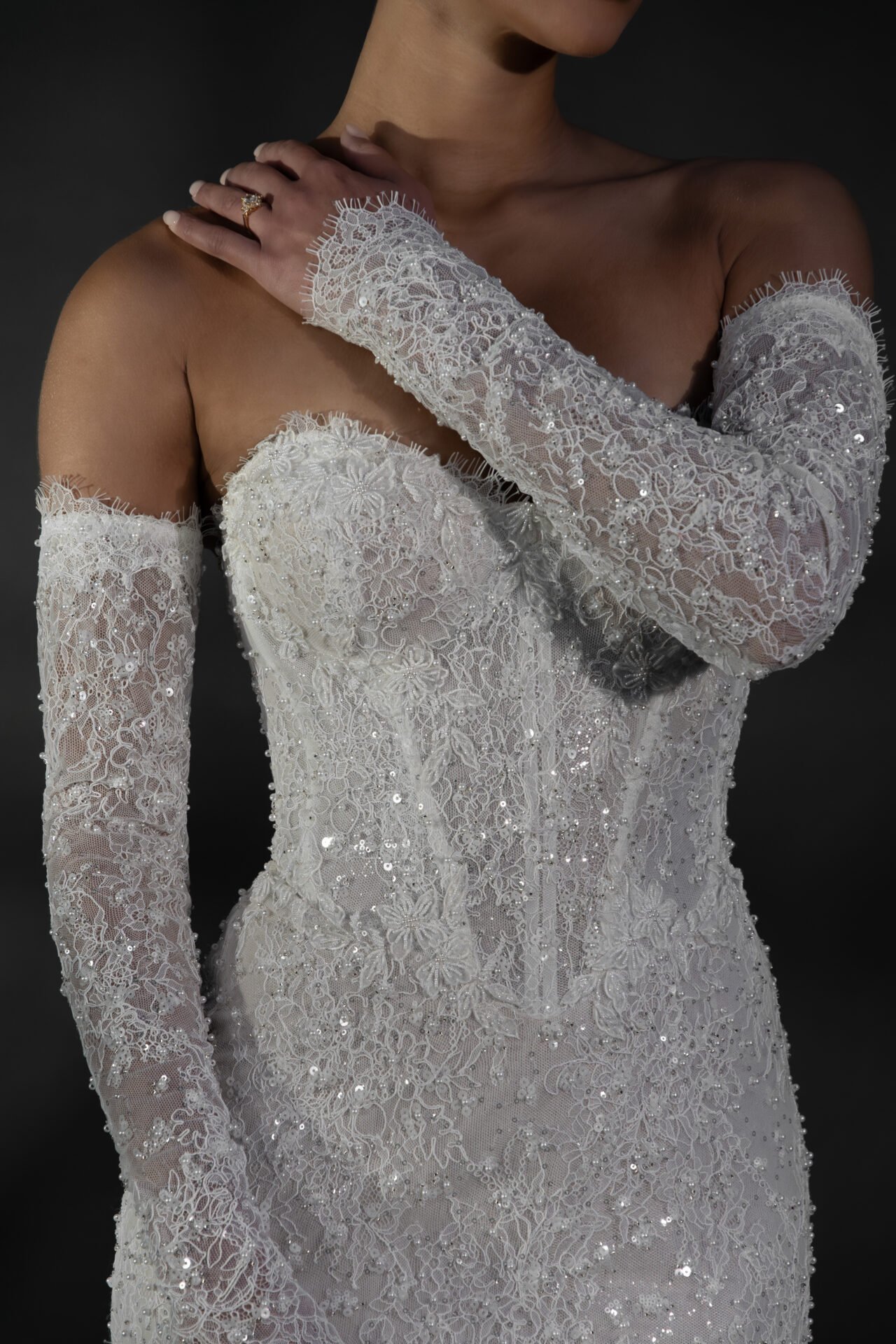 A woman in a white, lace, off-shoulder, sequined dress with matching lace gloves.