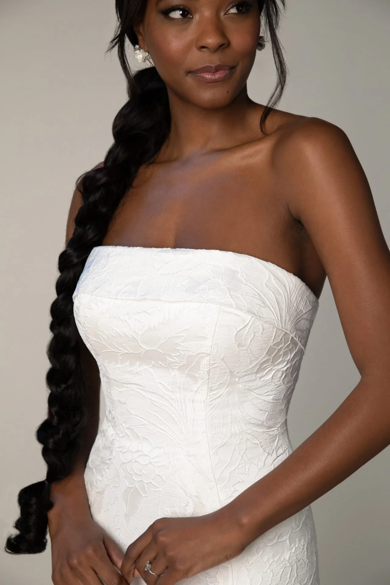 A woman in a strapless white dress with floral embroidery and long dark braided hair