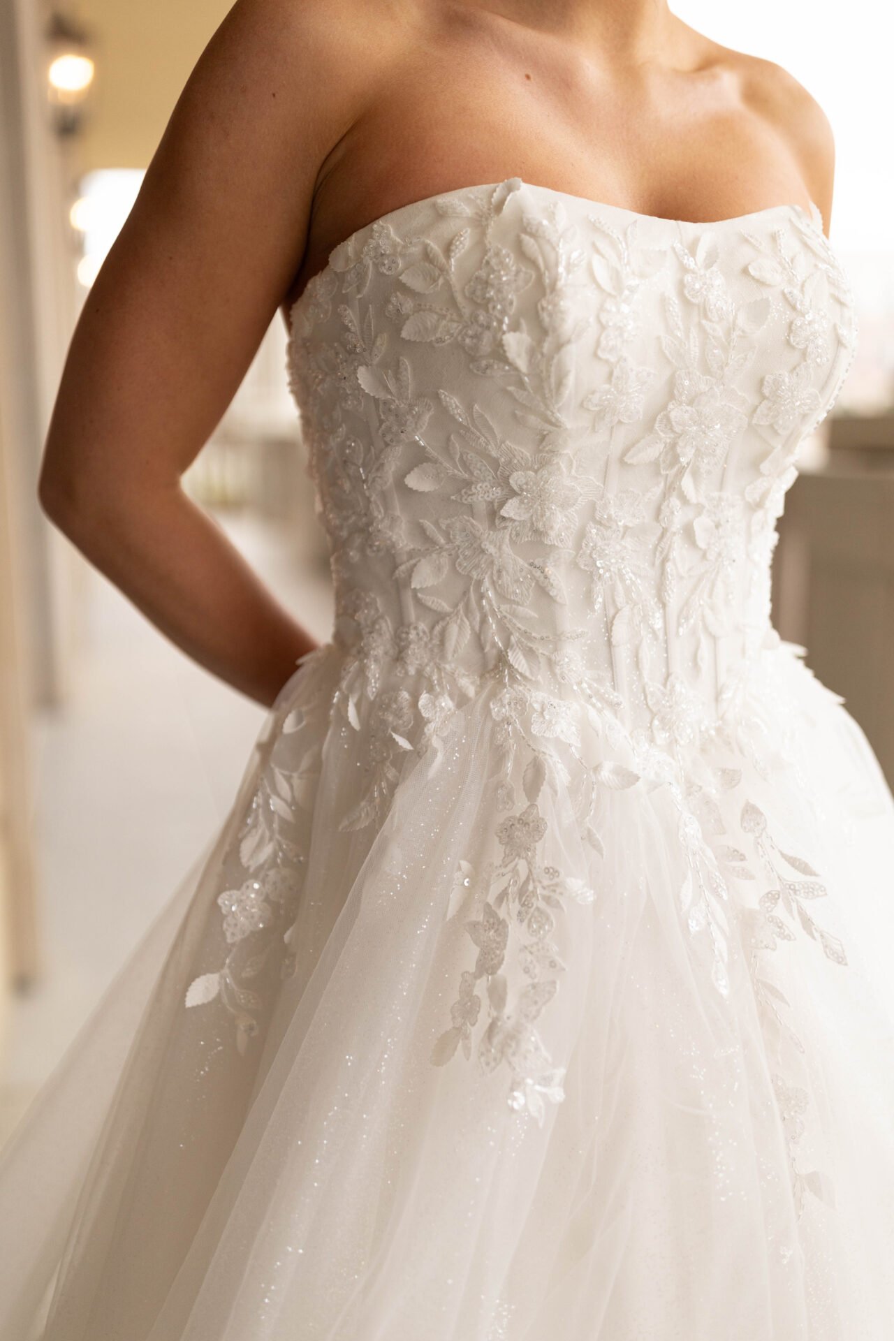 Close-up of a bride in a strapless white wedding gown with floral embroidery and lace details.