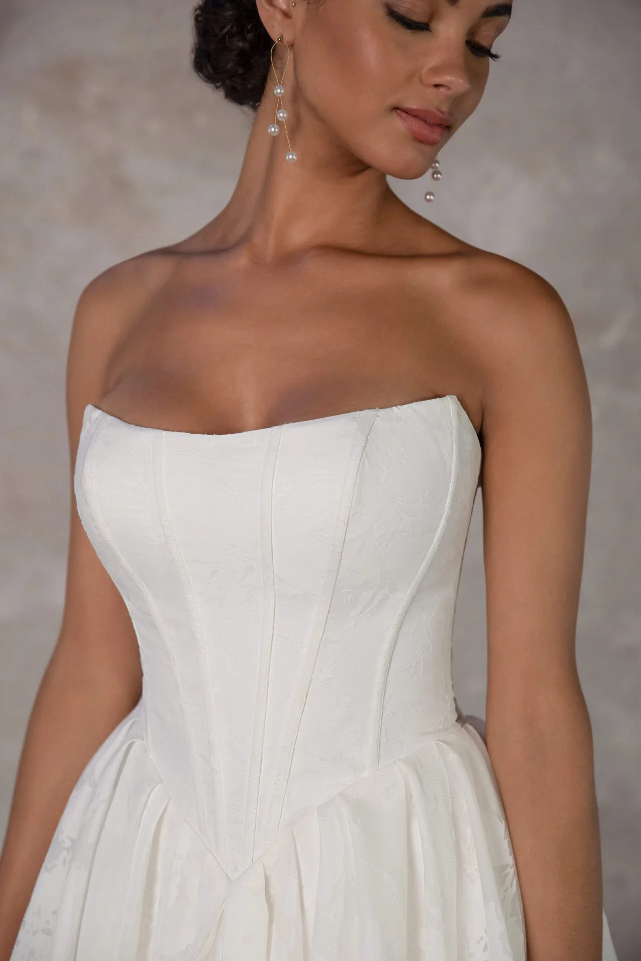Close-up of a woman wearing a strapless white dress with a structured bodice, accessorized with long pearl earrings.