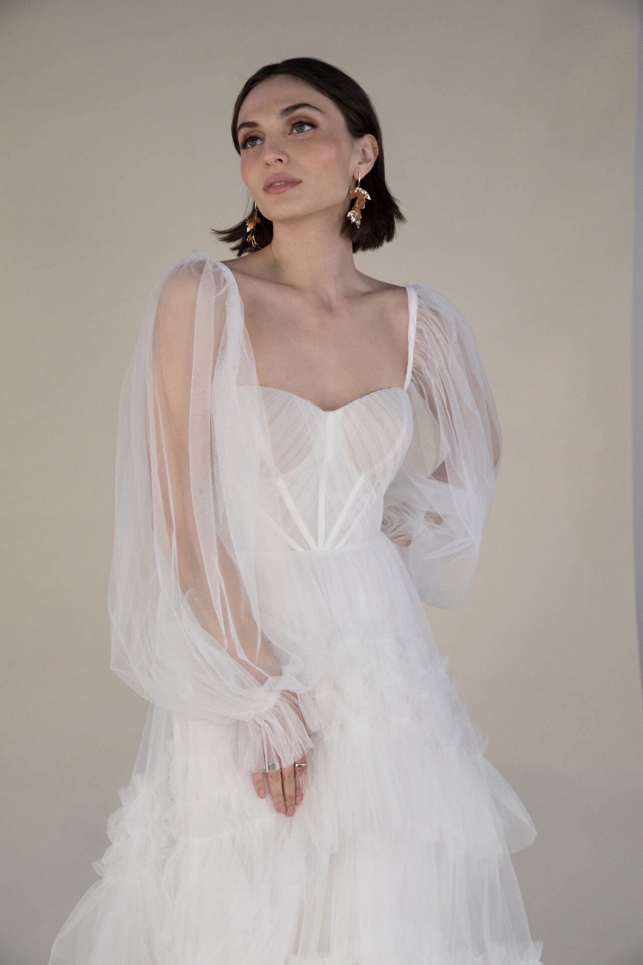 A woman in a white, strapless, layered dress with sheer puff sleeves and gold earrings.