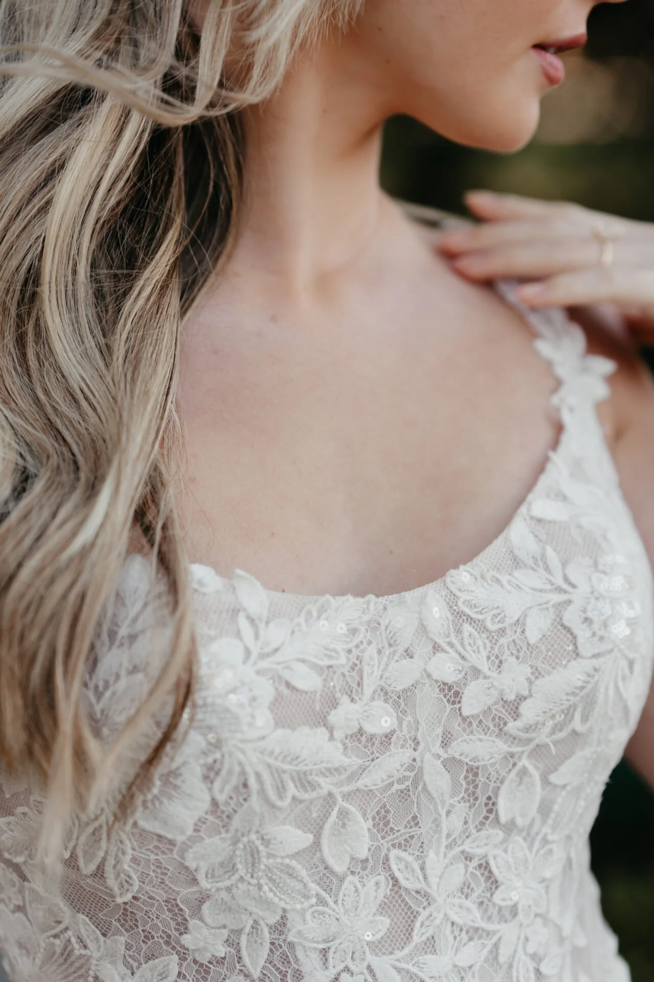 Close-up of a woman with long, wavy blonde hair wearing a white lace dress with floral embroidery.