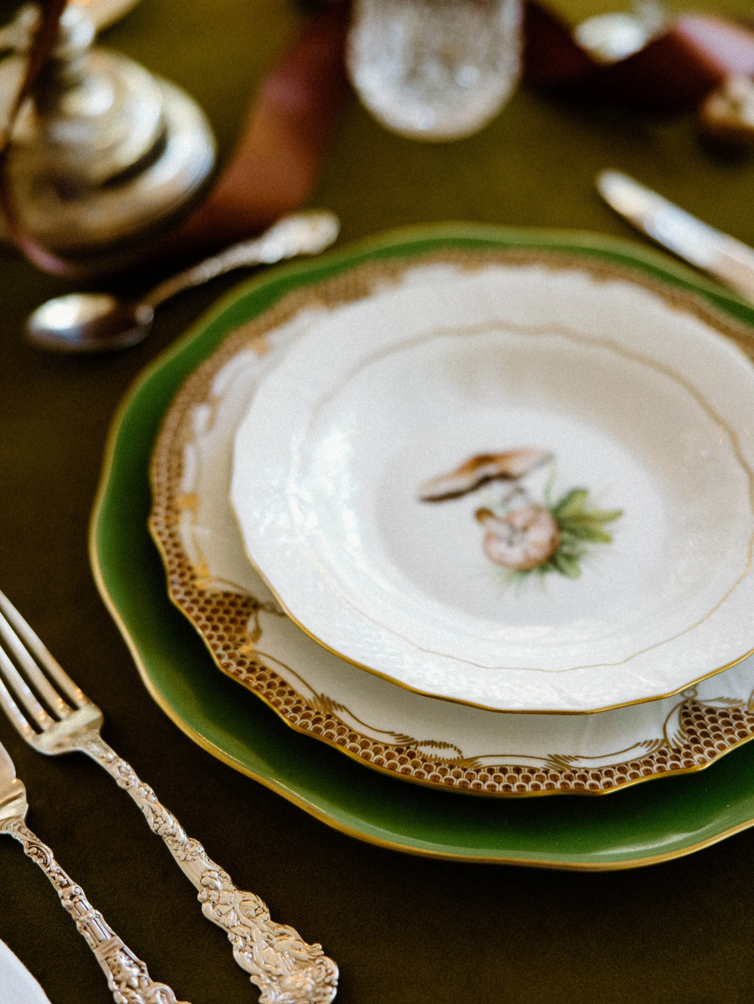 Elegant table setting with ornate china plates, silverware, and a dark tablecloth.
