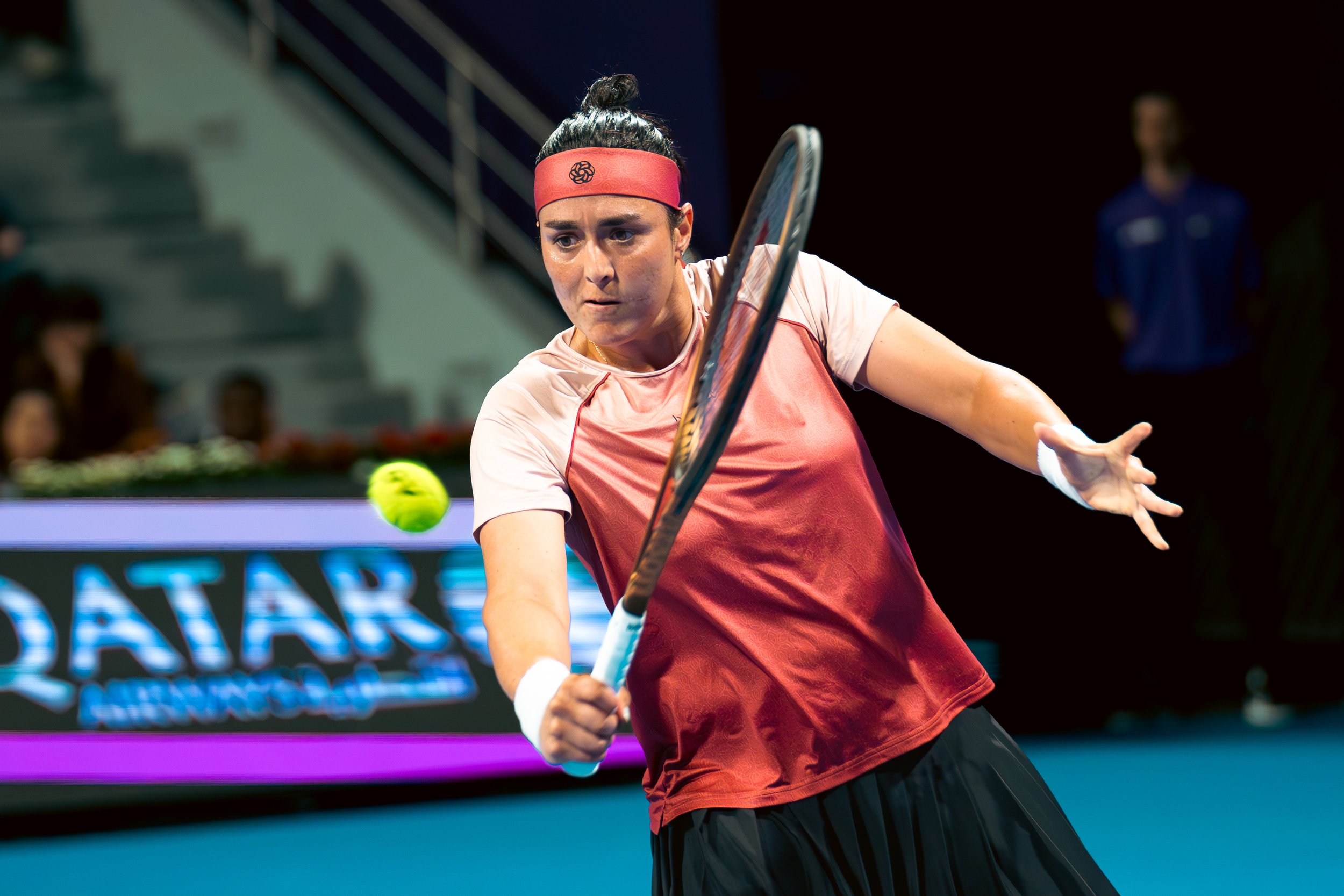 Female tennis player hitting a forehand shot on an indoor court with a yellow tennis ball in focus.