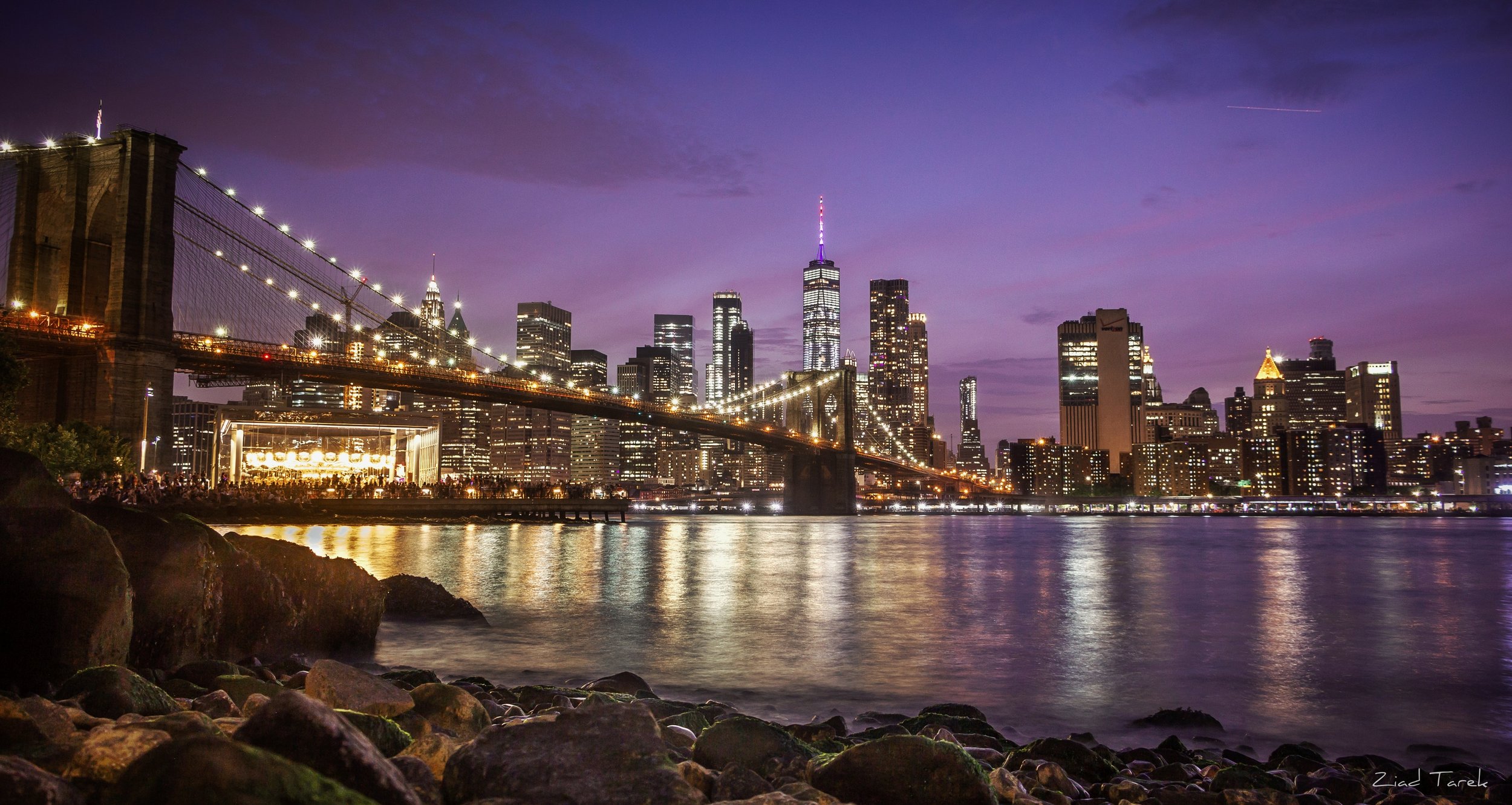 Stunning evening view of the Brooklyn Bridge with the illuminated New York City skyline in the background, reflecting on the East River.
