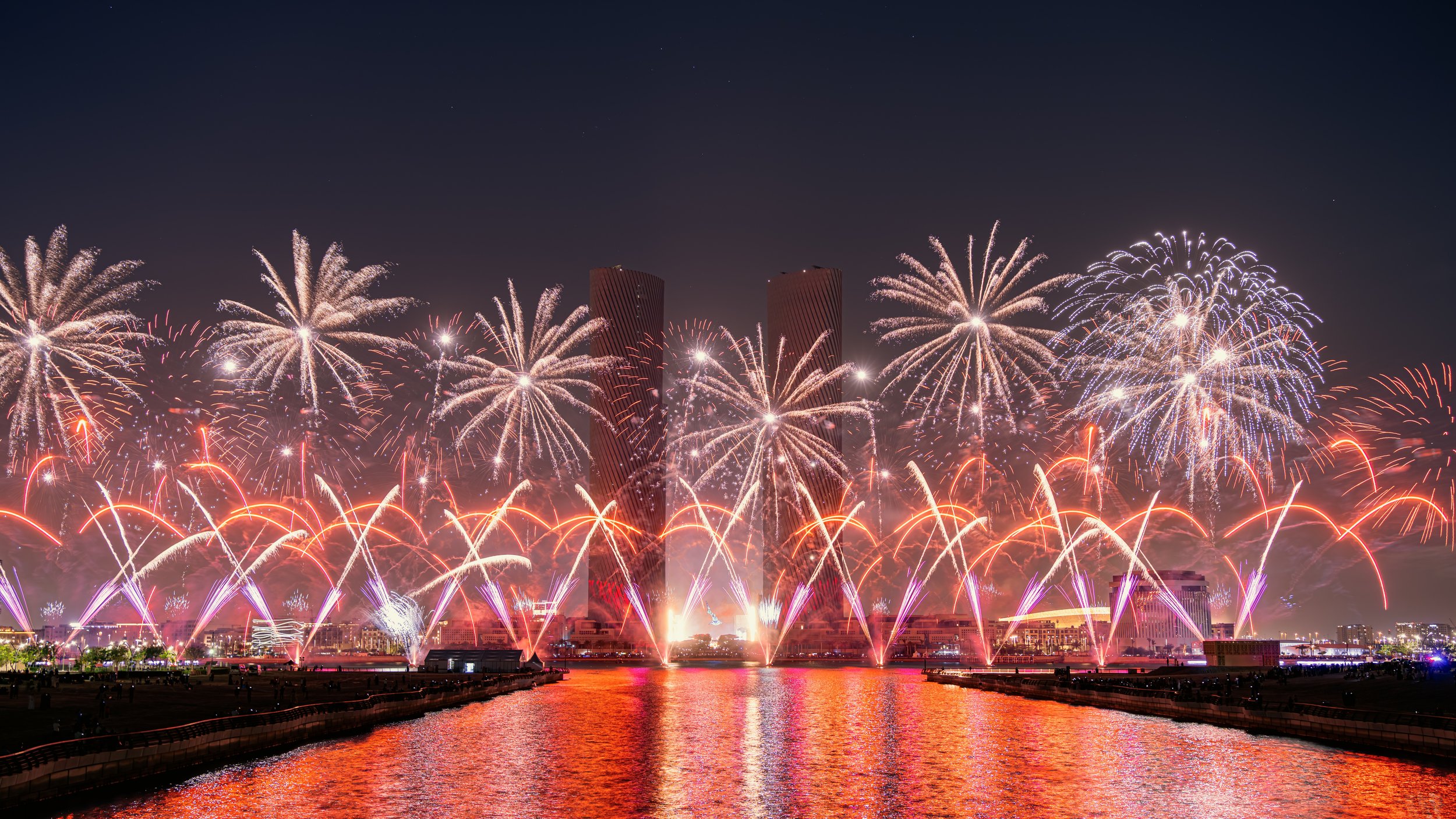 Colorful fireworks display over buildings and water at night.