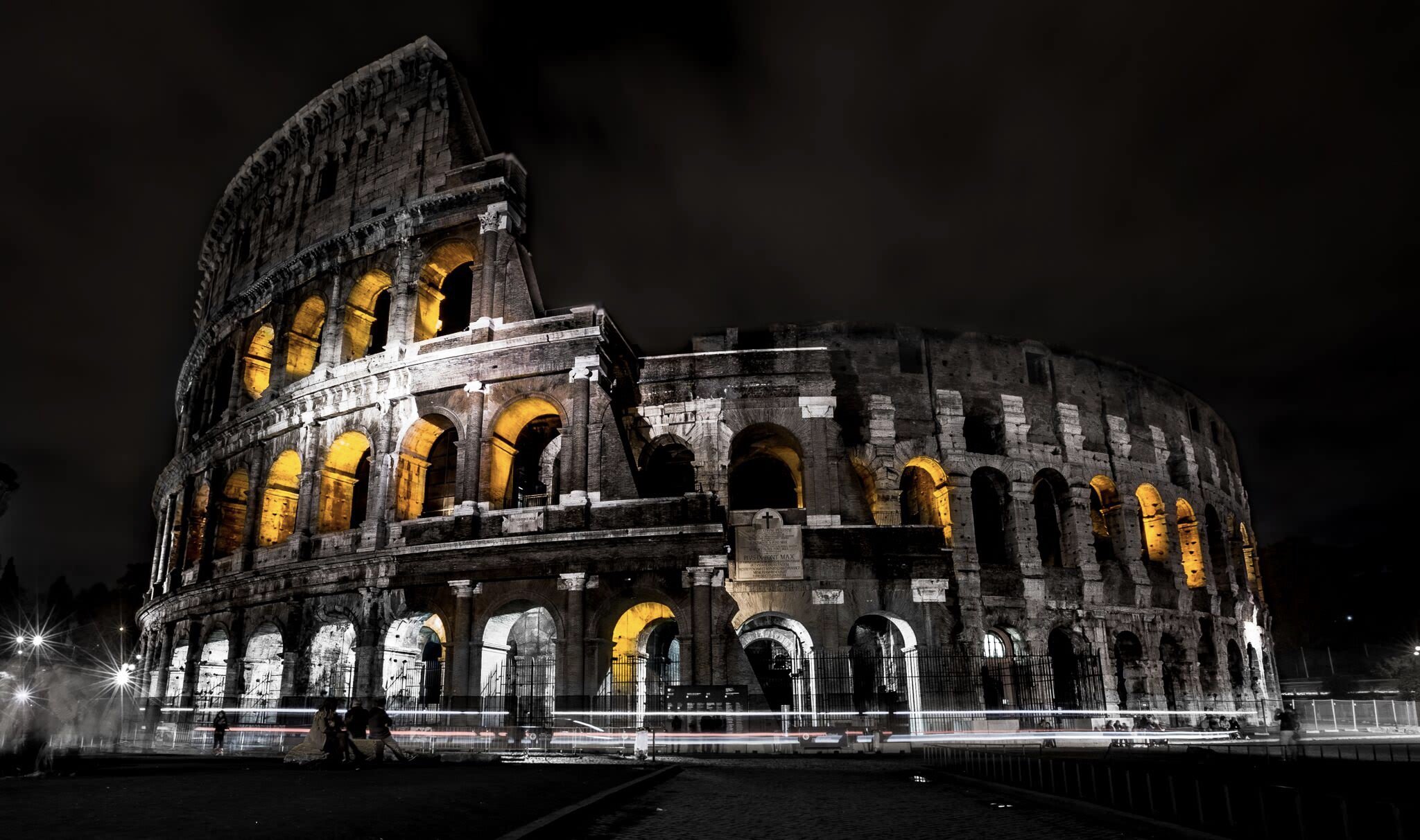 Night view of the Colosseum in Rome, Italy, illuminated with yellow lights highlighting the arches.