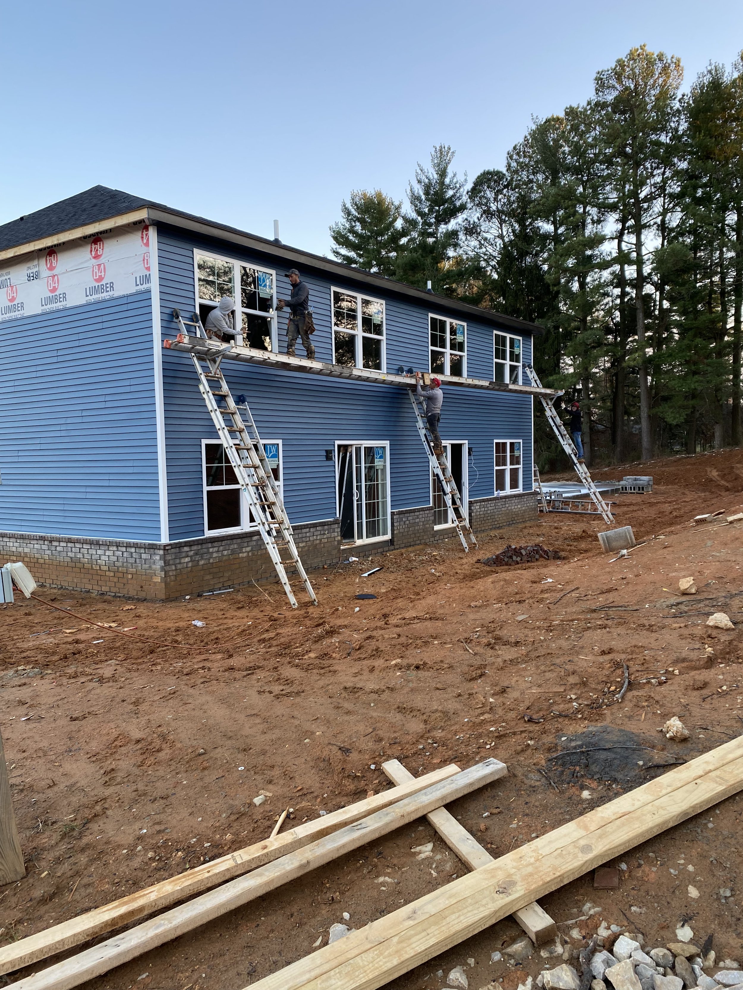 Workers installing windows on a two-story blue house under construction with ladders and scaffolding.