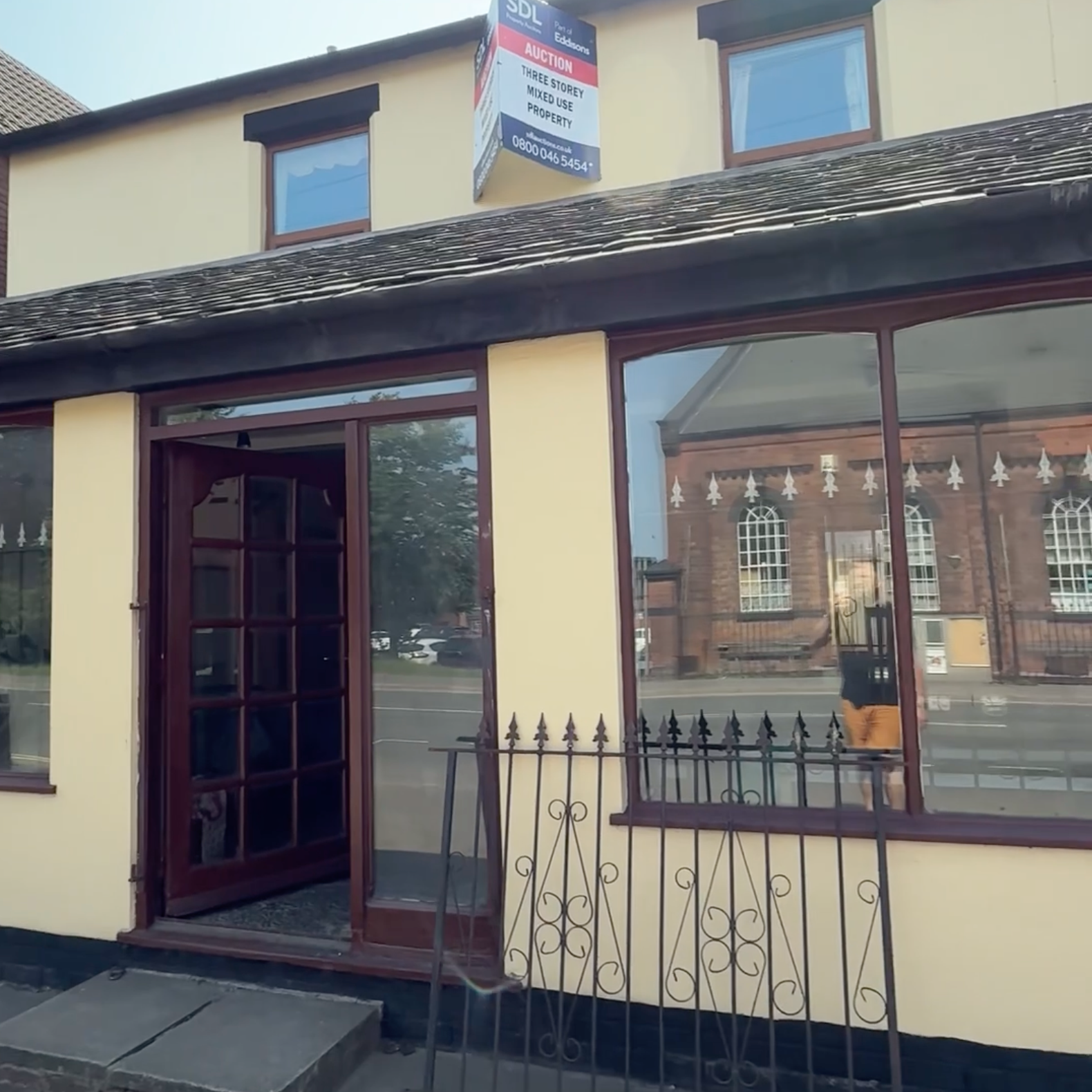 Exterior view of a commercial building with large windows and a glass door, a black iron fence, and a sign on top advertising an auction for a mixed-use property.