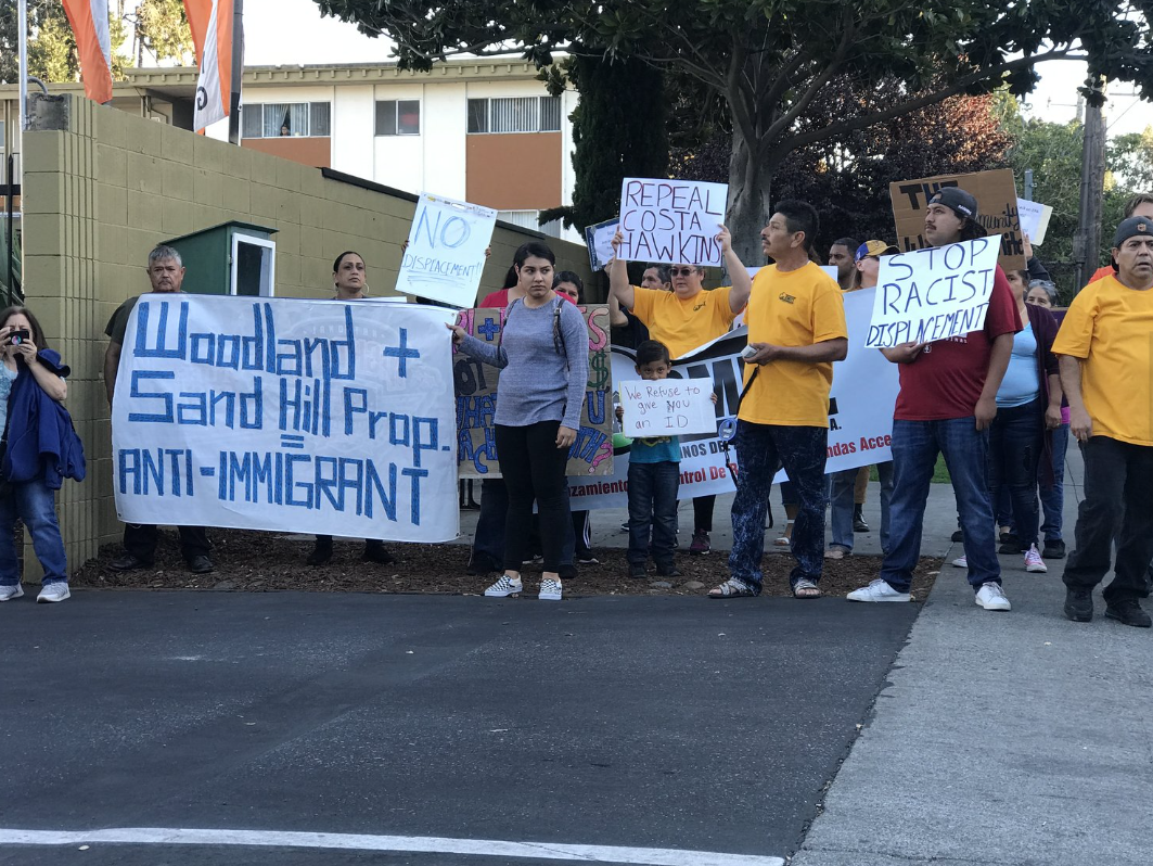 Group of people protesting with signs and banners demanding no displacement, stopping racist displacement, and advocating for anti-immigrant policies.