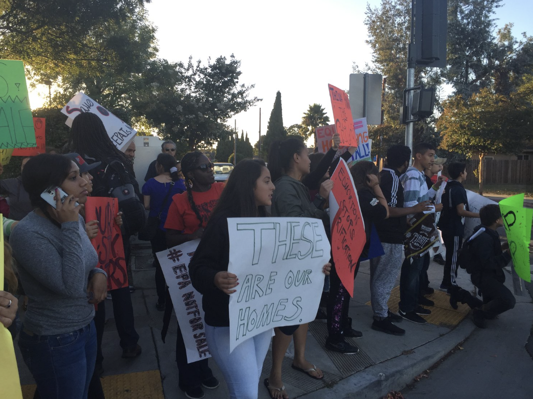 A group of people participating in a protest or demonstration on a sidewalk, holding signs with messages about social and environmental issues.