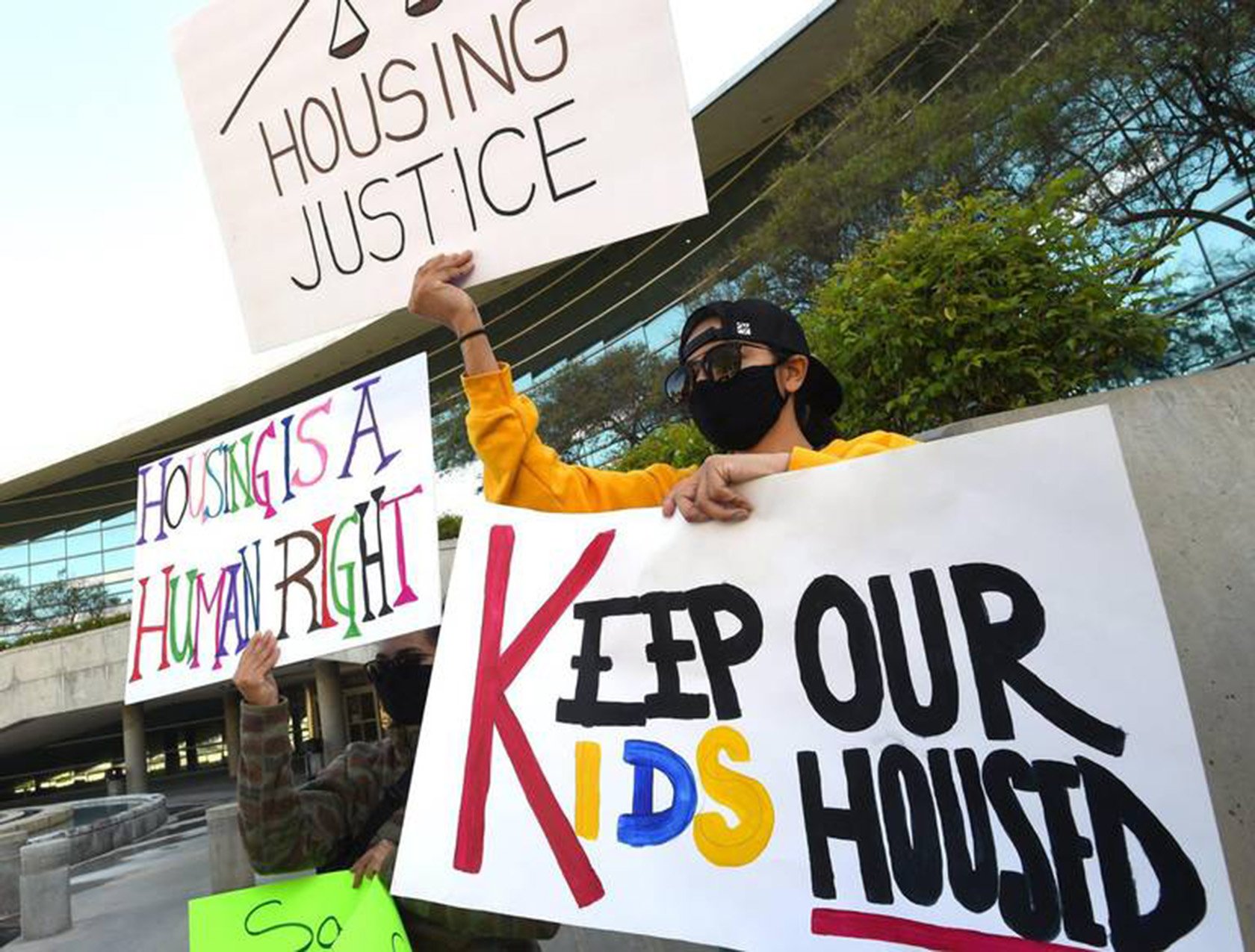 People participating in a protest holding signs with messages advocating for housing justice and protecting children's housing rights.