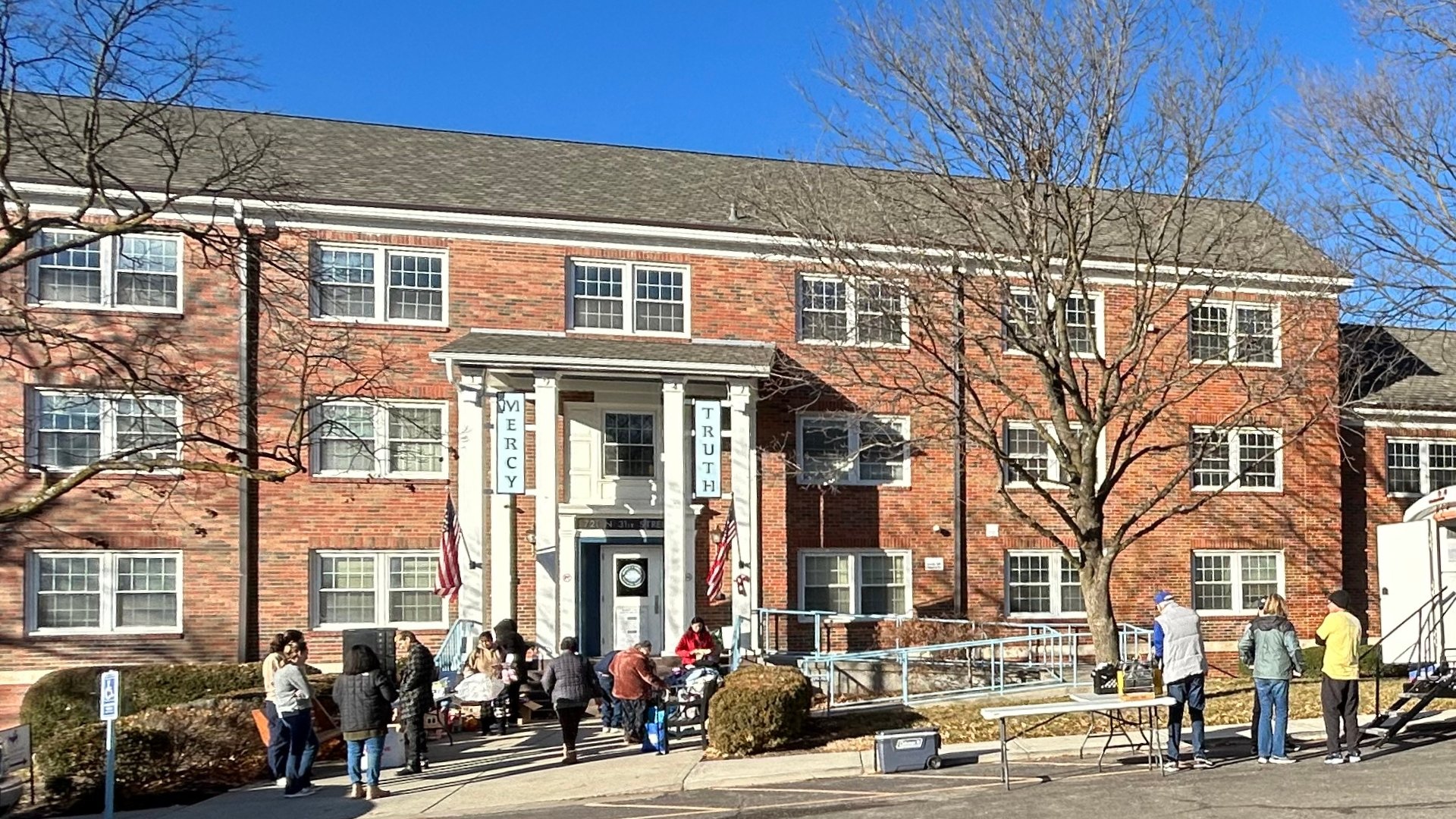 Mercy & Truth Healthcare Ministry in Kansas City, Kansas, with people gathered out front and American flags displayed on the building.