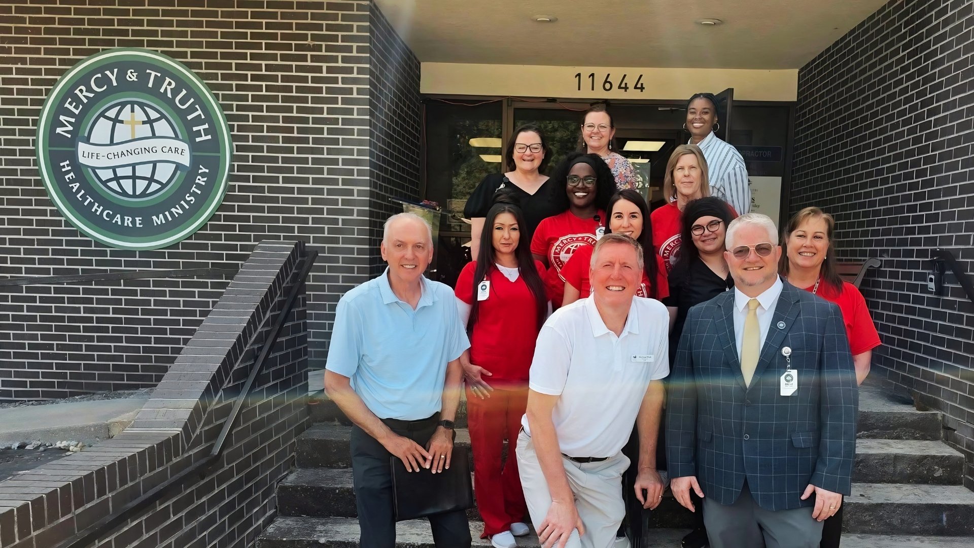 The Mercy & Truth Healthcare Ministry team standing together in front of their Shawnee, Kansas building, with the Mercy & Truth logo on the wall behind them.