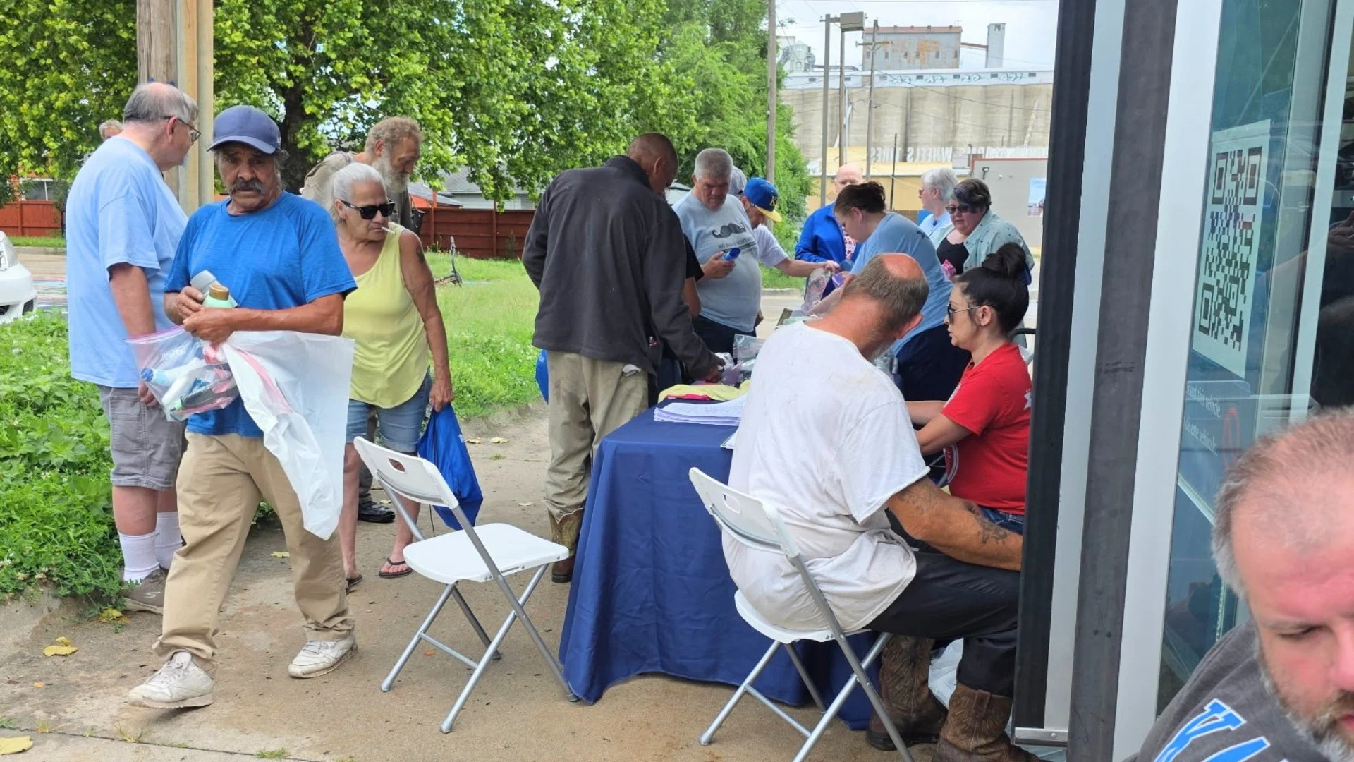 A Community Health Worker checks a man's vitals at the Mobile Health Clinic while neighbors carry free supply bags at June's F.I.R.S.T. Tuesday.