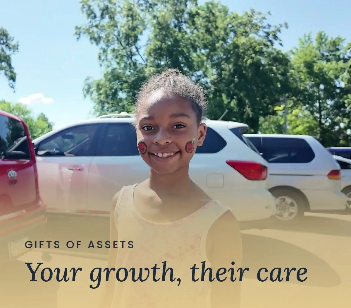 A smiling young girl with face paint enjoys a Mercy & Truth community event in Kansas City. Text reads "Gifts of Assets: Your growth, their care."