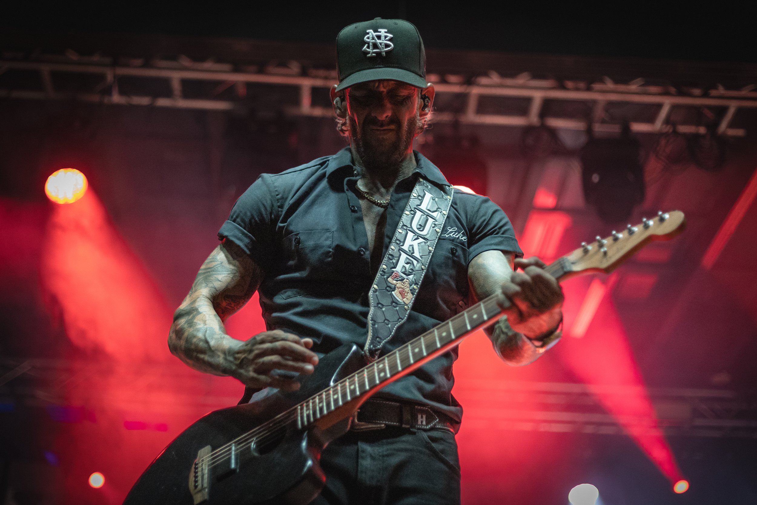 Musician playing guitar on stage with red stage lighting.