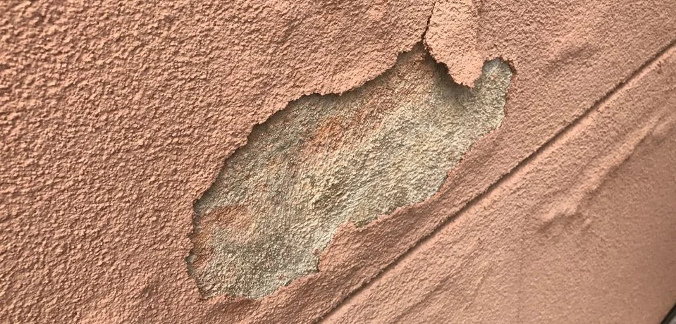 Damaged exterior stucco with peeling paint and moisture bubbling on a residential wall in Buckeye, AZ.