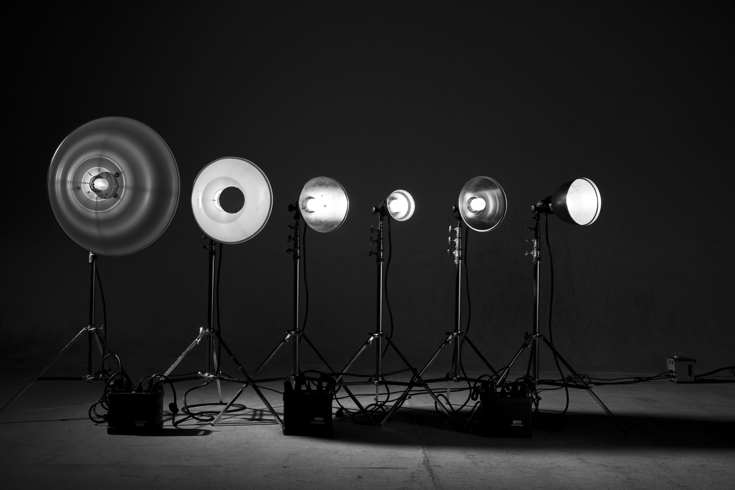 Multiple studio lights on stands arranged in a row against a dark background.