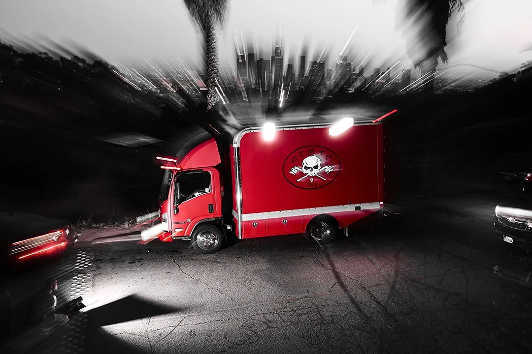 A red food truck with a skull logo parked on a dark street at night, with motion blur effect around the image.