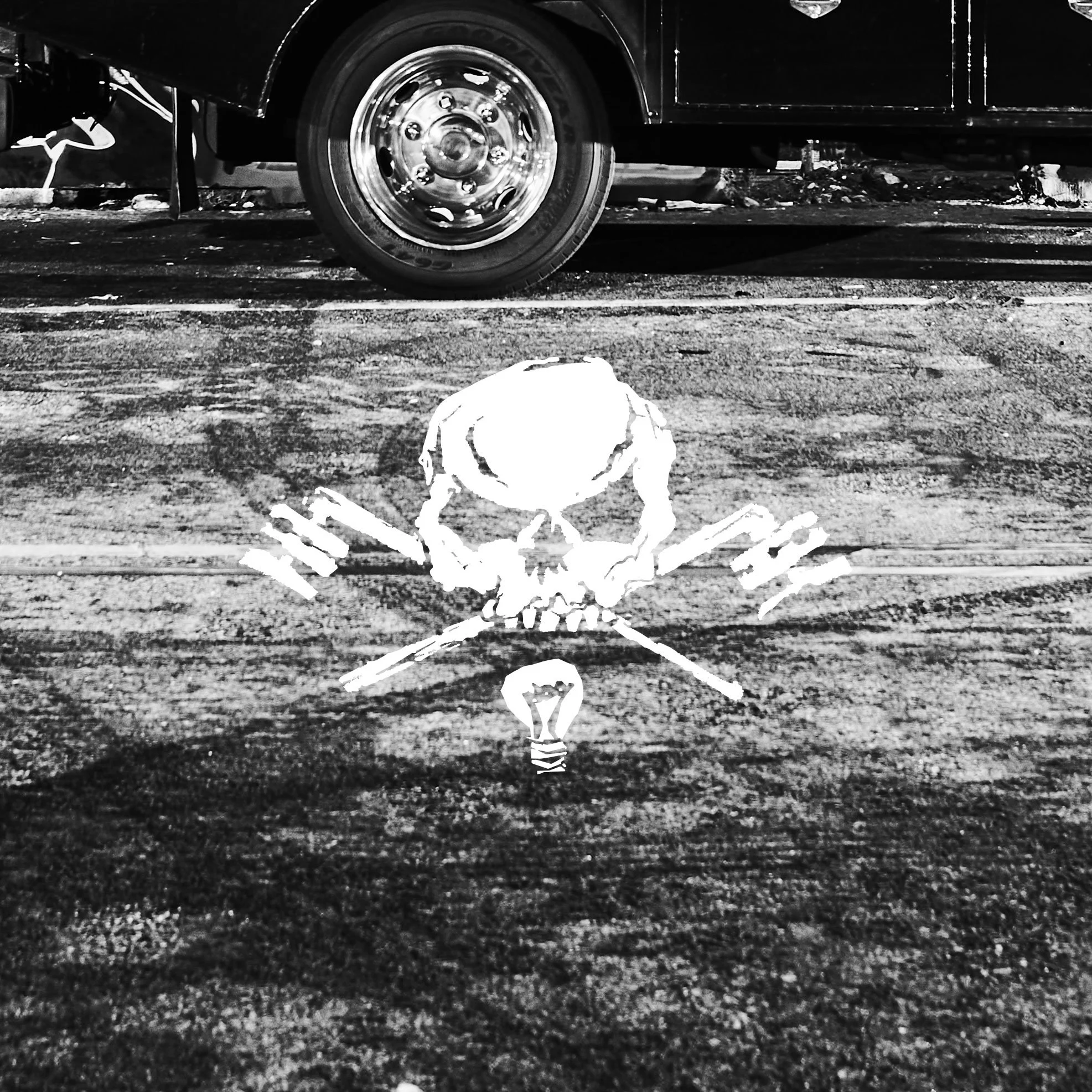 Black and white photo of a car's front wheel and body with a skull and bones illustration painted on the ground beneath it.