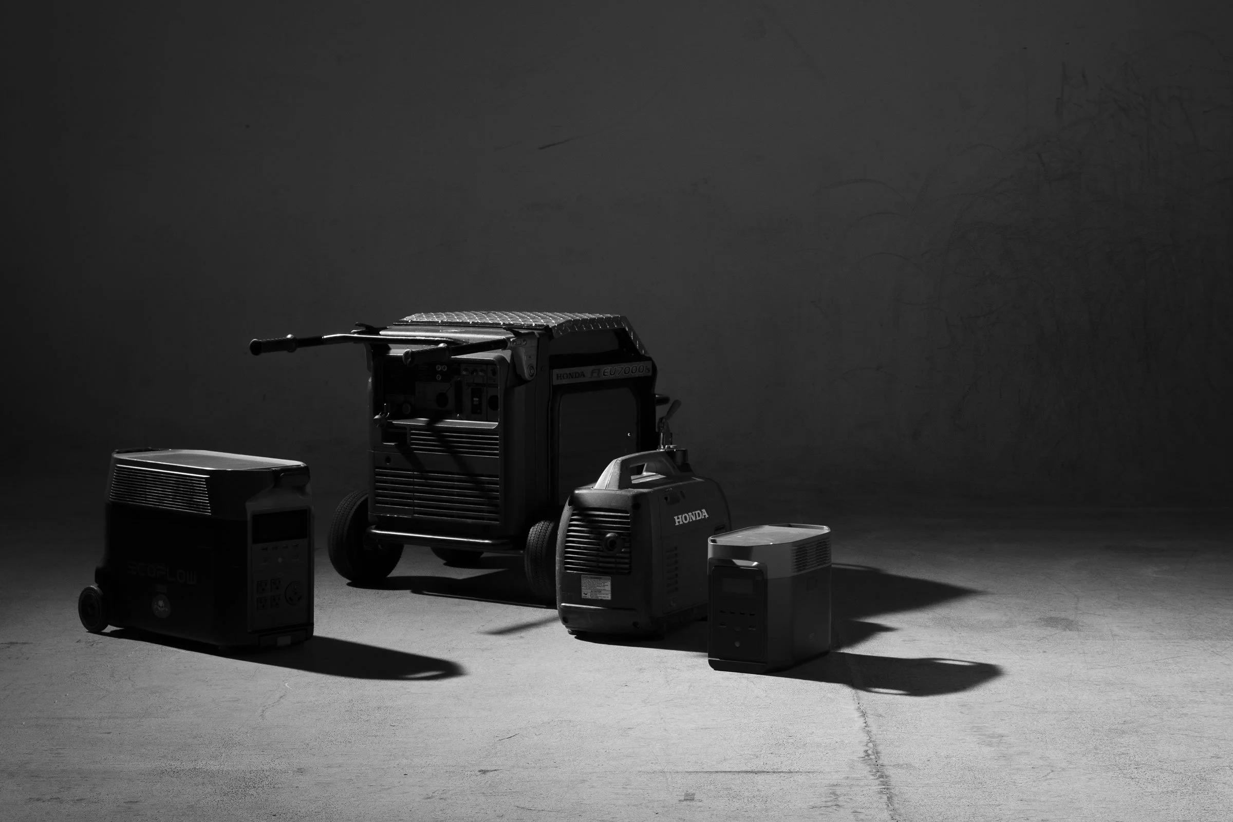 Various black and gray power tools and battery chargers are arranged on a dark surface with a plain dark background.