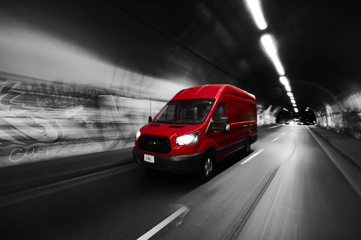A bright red van driving through a tunnel with graffiti on the walls, with a black-and-white background showing motion blur.
