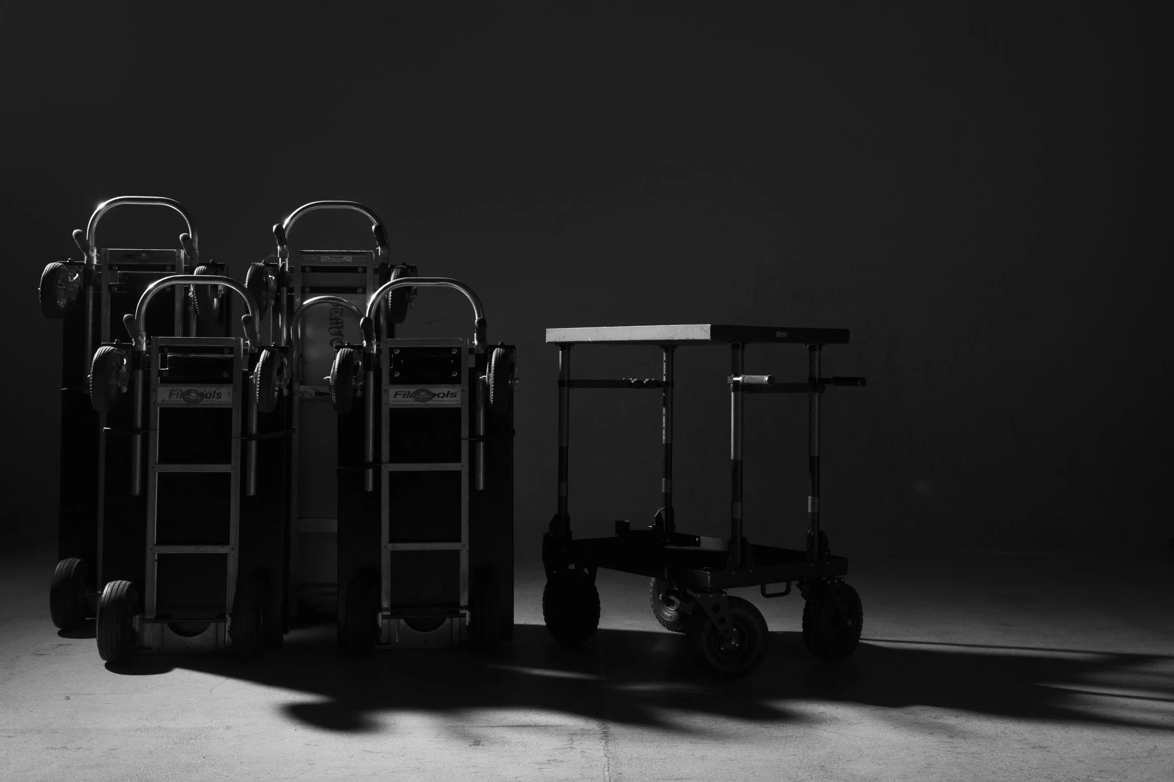 Black and white image of medical or laboratory equipment, including carts with wheels and various tools, set against a dark background.