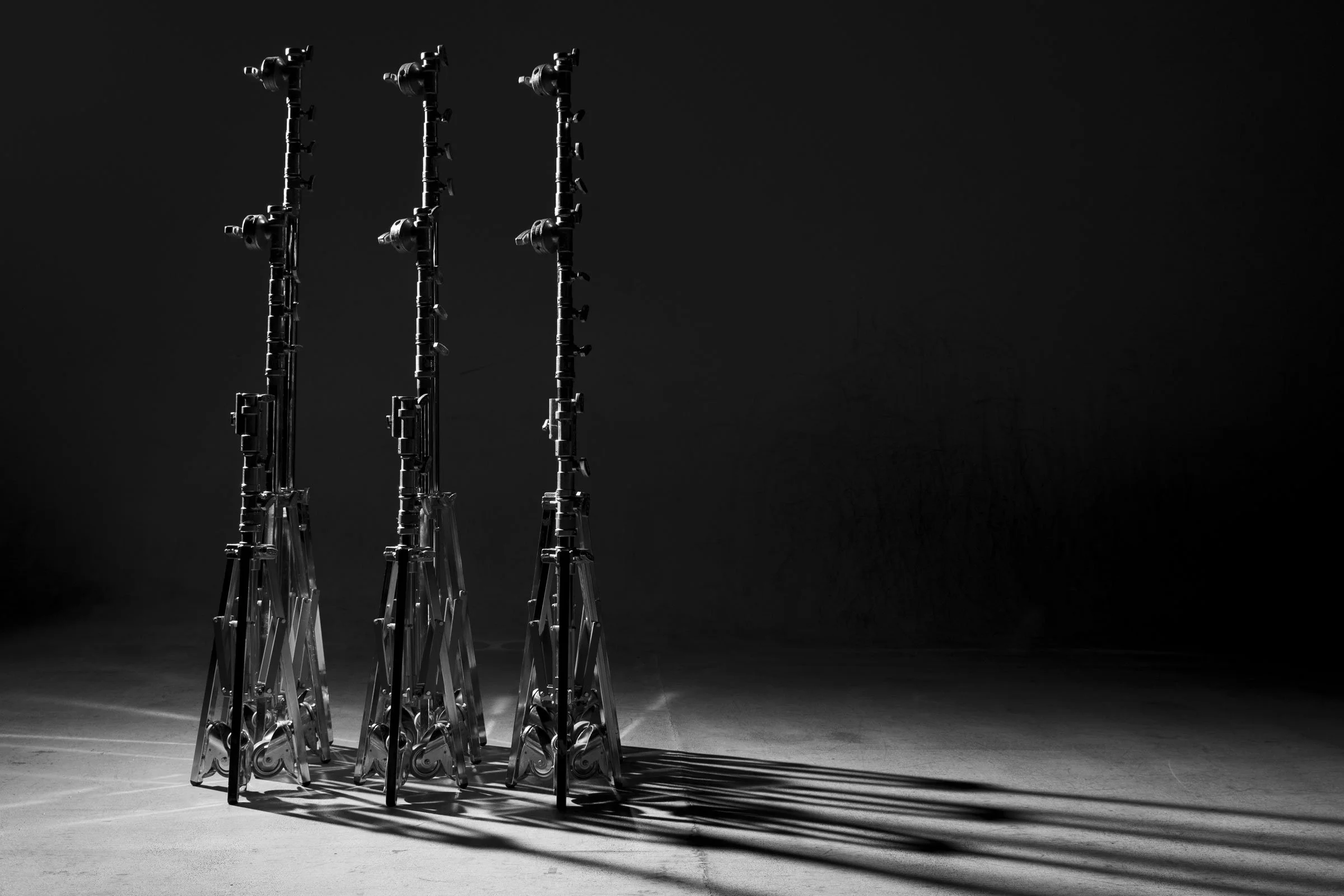 A group of four metal scaffoldings arranged in a row on a dark studio background, casting distinct shadows on the floor.