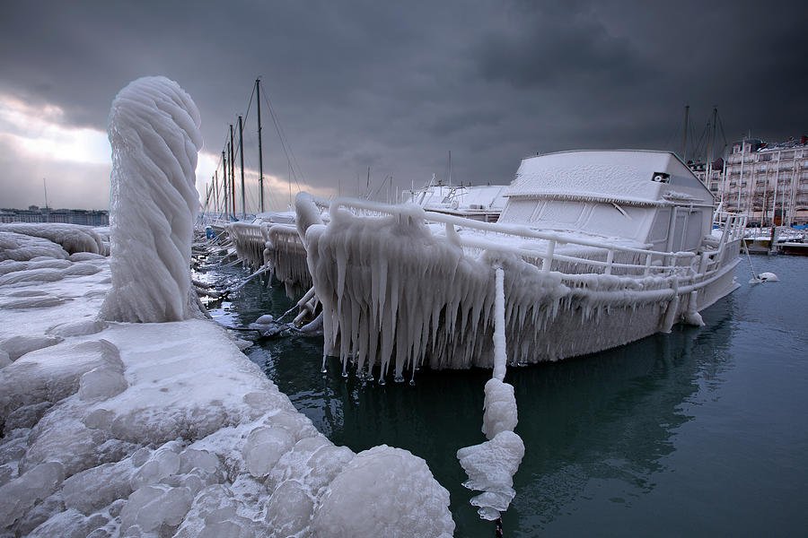 Boat covered and frozen in ice at a harbor during winter, with ice formations on the dock and boat.