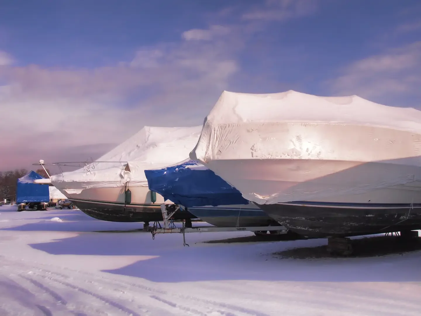 A boat covered with snow and ice on a snowy ground, with another boat covered with snow in the background, under a cloudy sky.