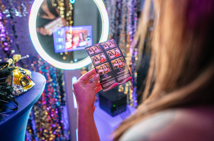 Person holding a photo strip from a photo booth with a built in ring light. Sequined backdrop and props are visible in the background.