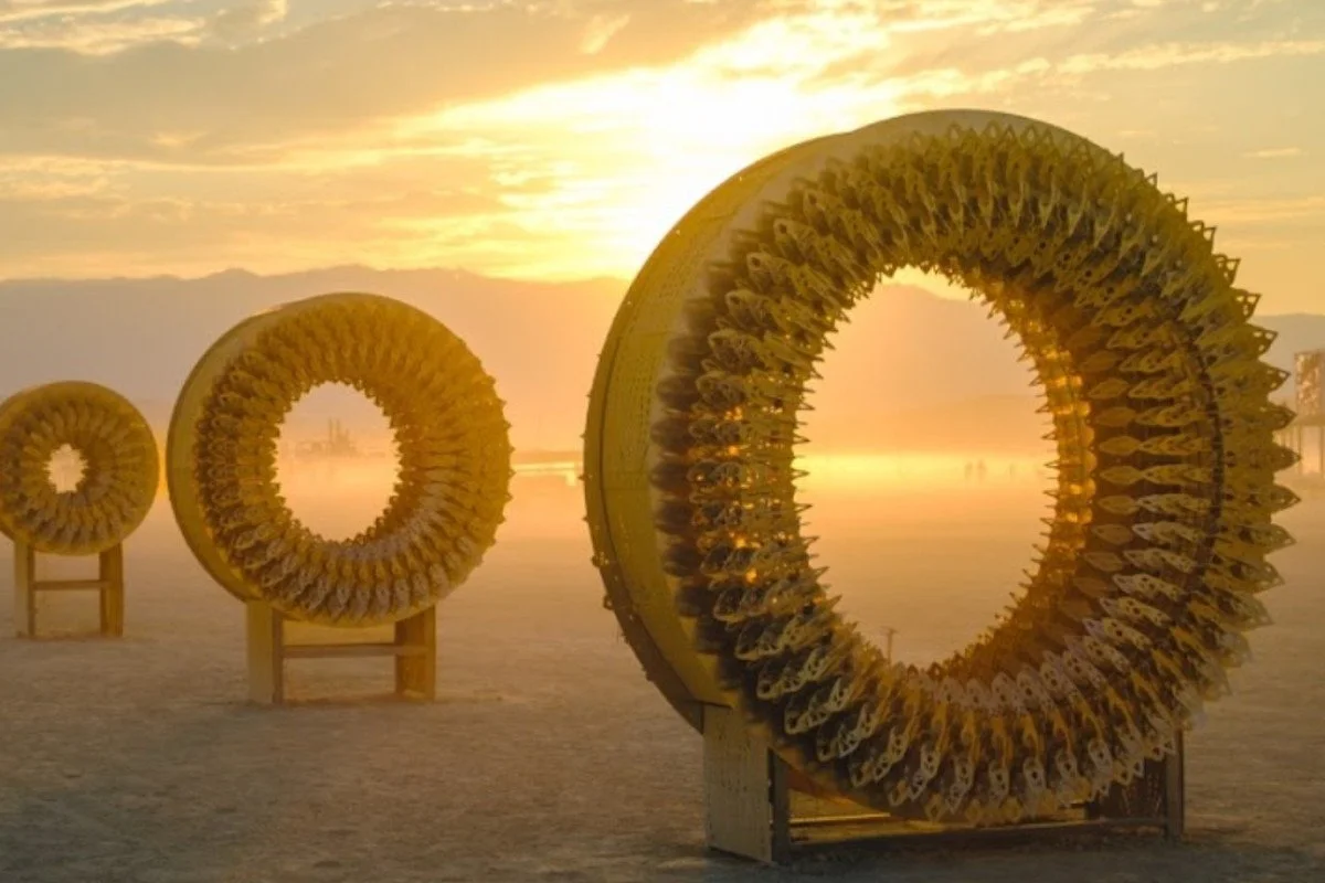 Three laser-cut ring sculptures of increasing size standing on the open playa at sunrise, sunlight glowing through the largest one.