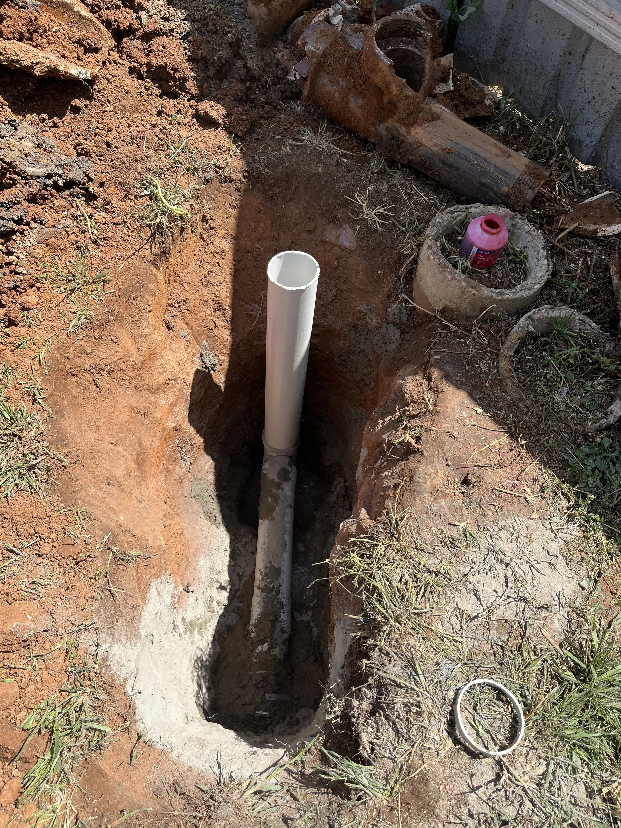 A vertical pipe installed in a freshly dug trench in the ground, with construction tools and materials around it.