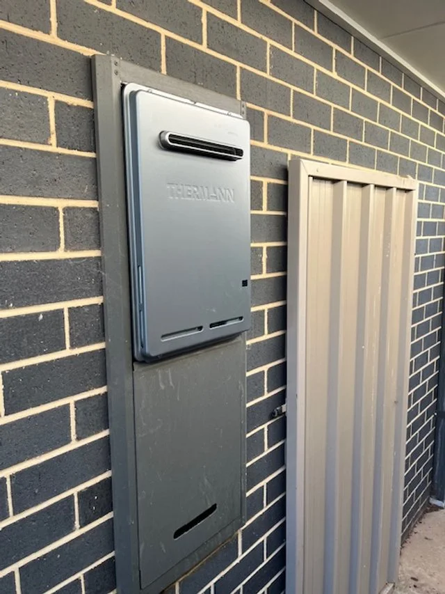 An outdoor electrical panel and a metal utility box mounted on a brick wall.