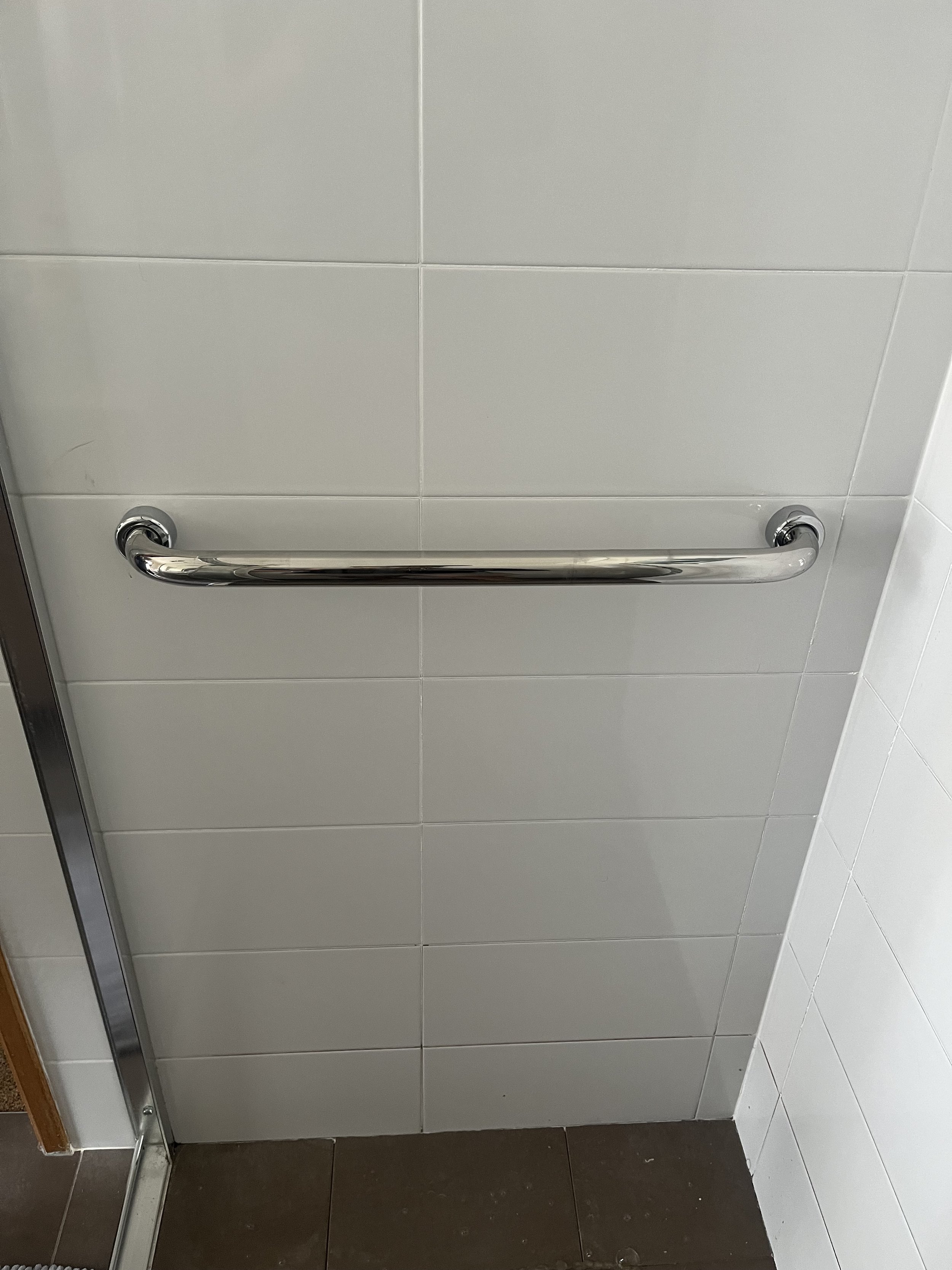 A metal grab bar mounted on a tiled bathroom wall.