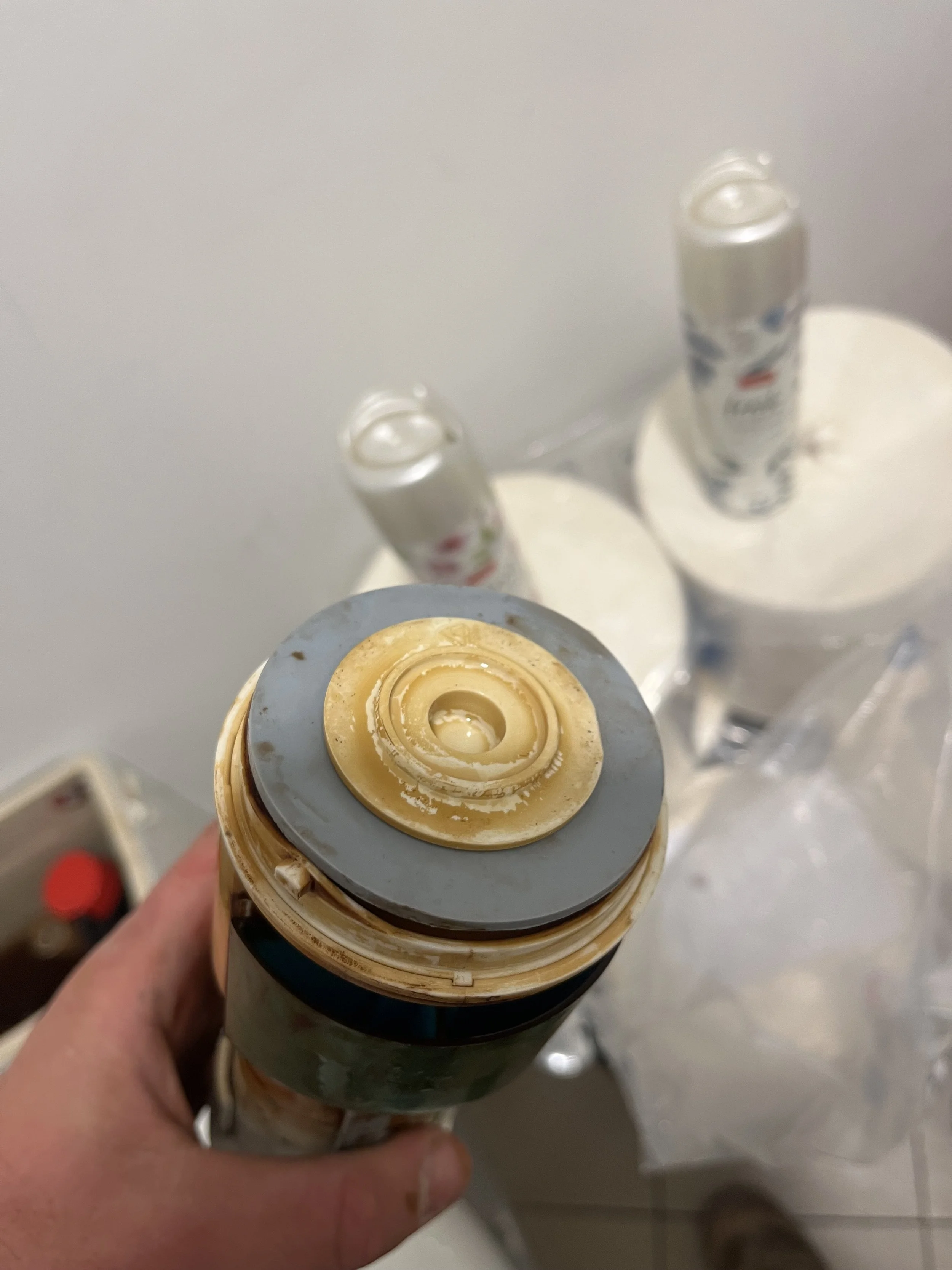 Close-up view of a hand holding a partially used can of spray foam insulation, with two other aerosol cans in the background on top of white paper towels.