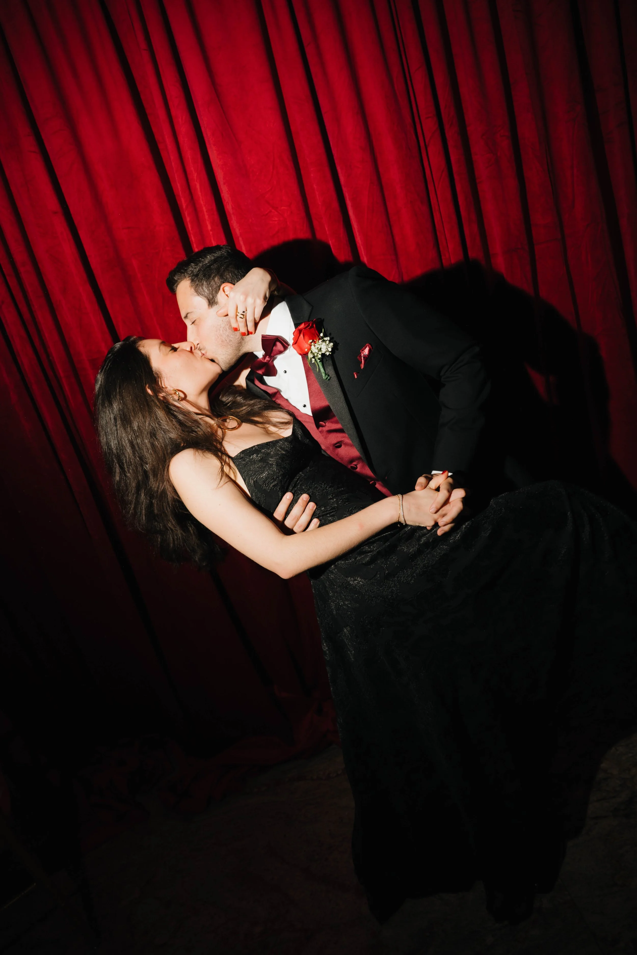 Wedding guest portraits in New Jersey featuring a couple sharing a romantic dip and kiss in front of a dramatic red velvet curtain during an editorial-style wedding portrait experience by Parado Studios.