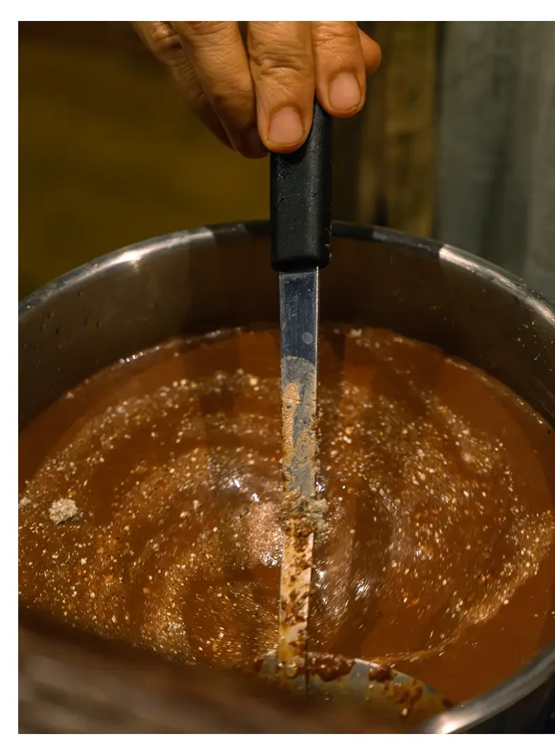A person's hand stirring a pot of hot chocolate or melted chocolate with a metal spoon.