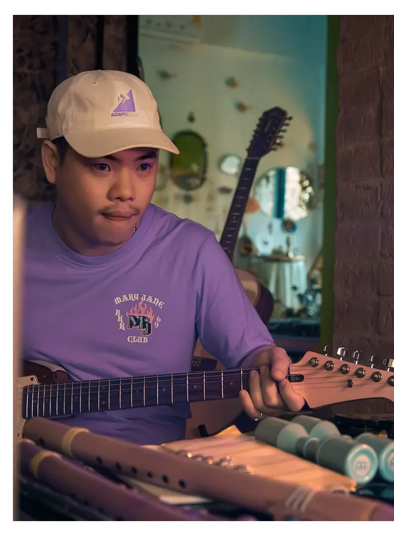 Young man playing an electric guitar in a cozy room with colorful decor and a brick wall.