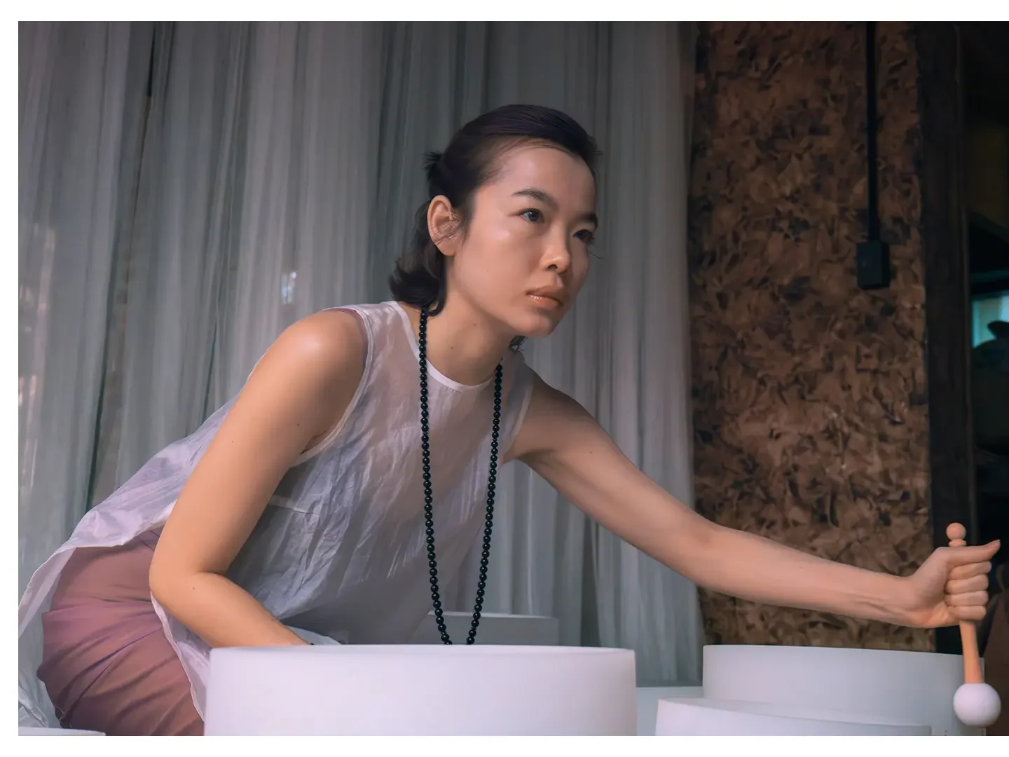 A woman with dark hair playing a musical instrument in a room with curtains and wooden wall.