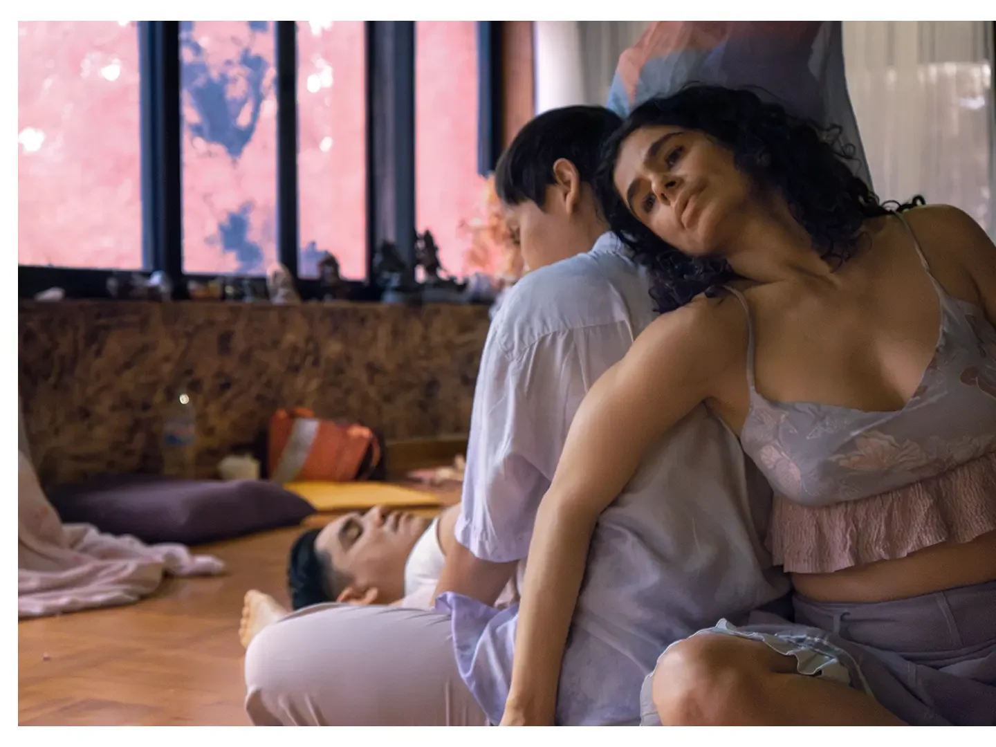 A woman leaning against a man with her eyes closed and a peaceful expression, while their friend lies asleep on the floor nearby.