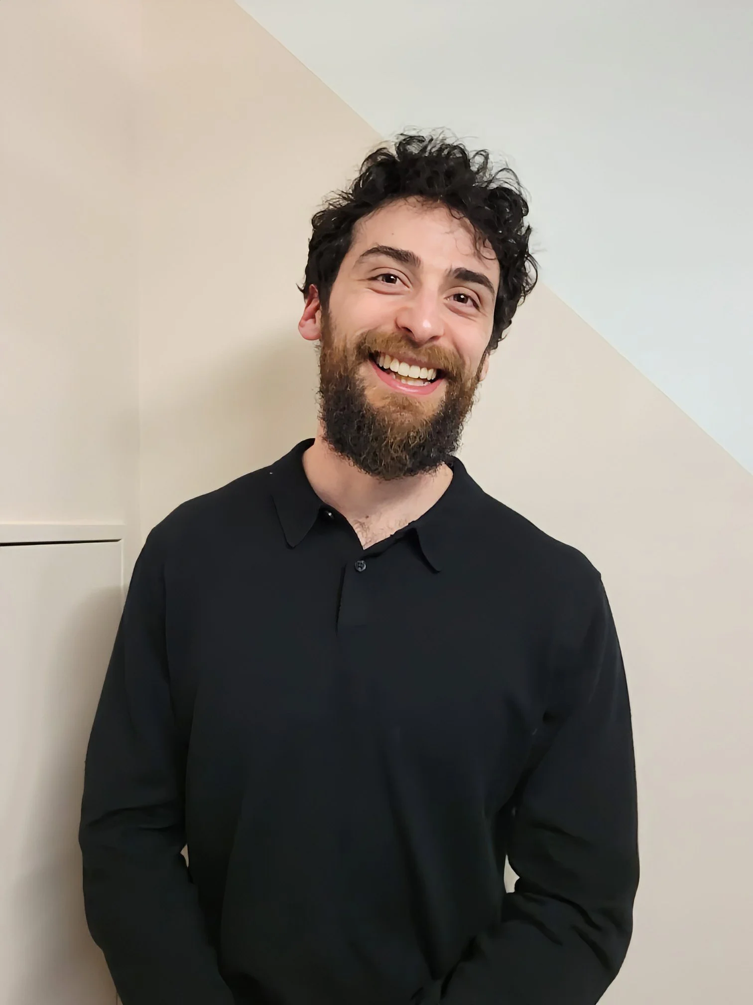 Julian, founder of Craft Fitness Studio, with curly dark hair and beard wearing a black shirt, standing in front of a beige-pink wall in his personal training studio in Karori, Wellington, New Zealand.