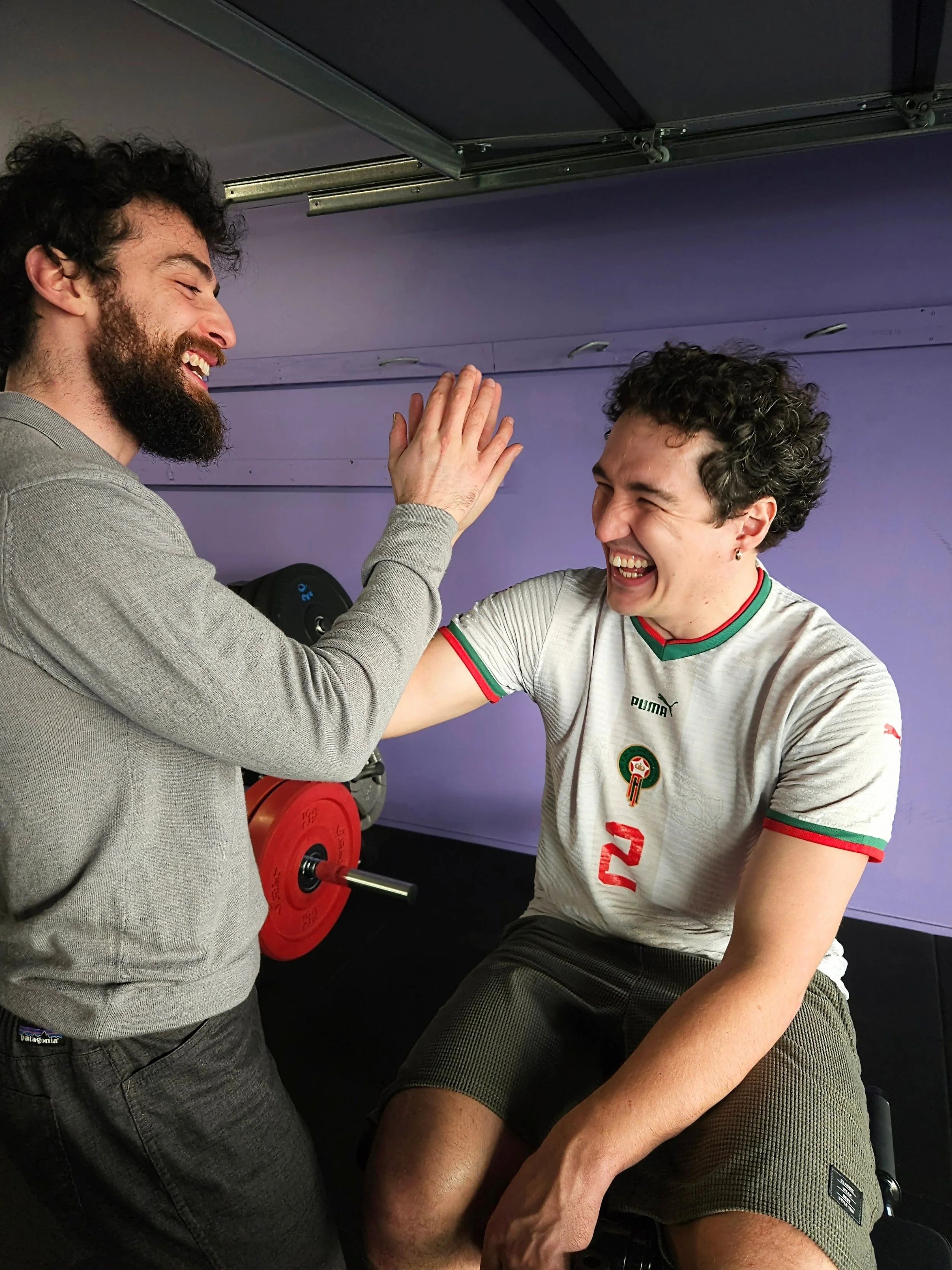A man using the REP Leg Extension & Leg Curl Bench Attachment, smiling and high-fiving with Julian, founder of Craft Fitness.