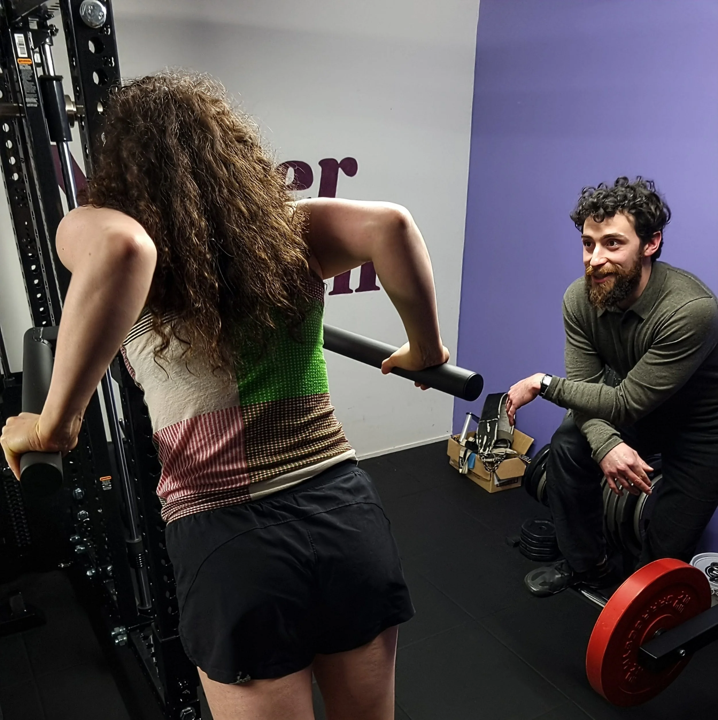 A local Karori woman with curly hair doing a dip using the REP Dip Station Attachment, while being trained by Julian Etchegoin, founder and personal trainer at Craft Fitness Studio.
