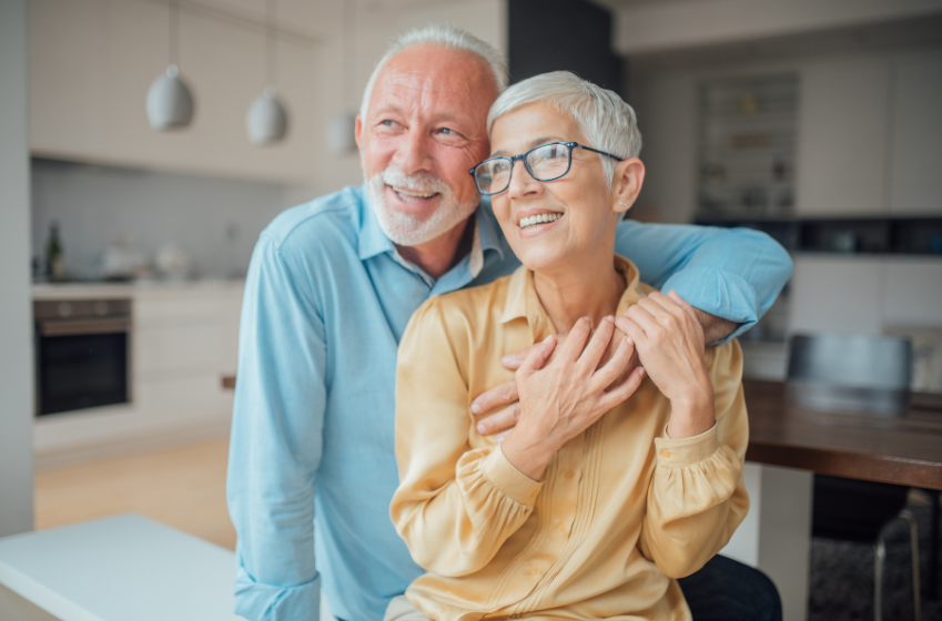 A happy elderly couple sharing a warm moment in a modern kitchen, smiling and embracing each other.