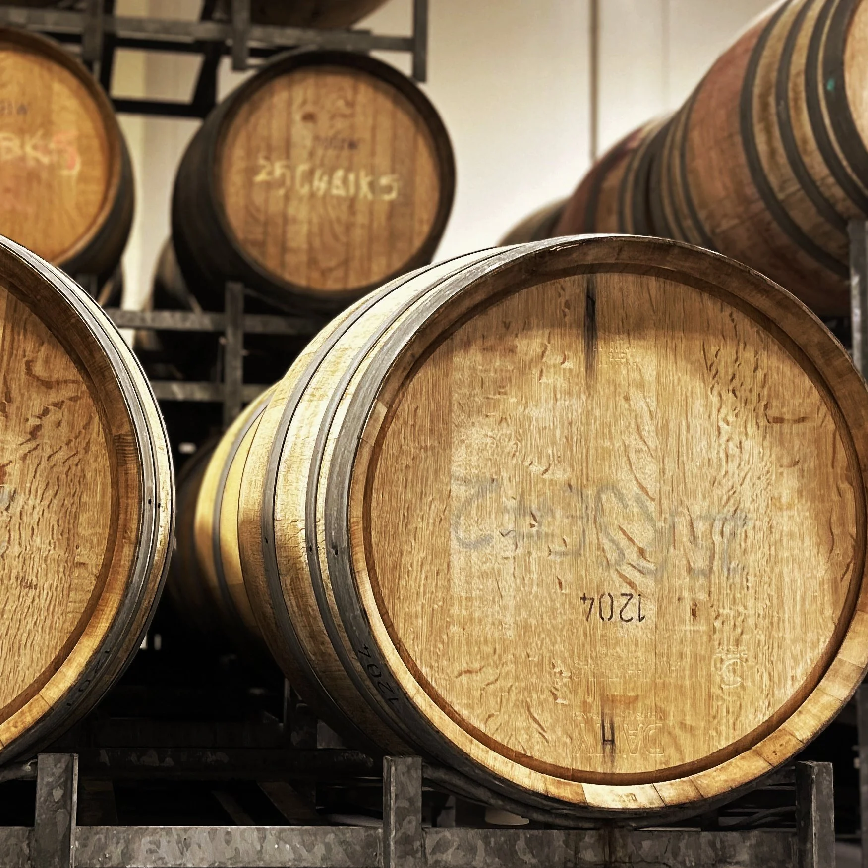 Wooden barrels stacked on metal racks in a wine cellar or brewery storage area.