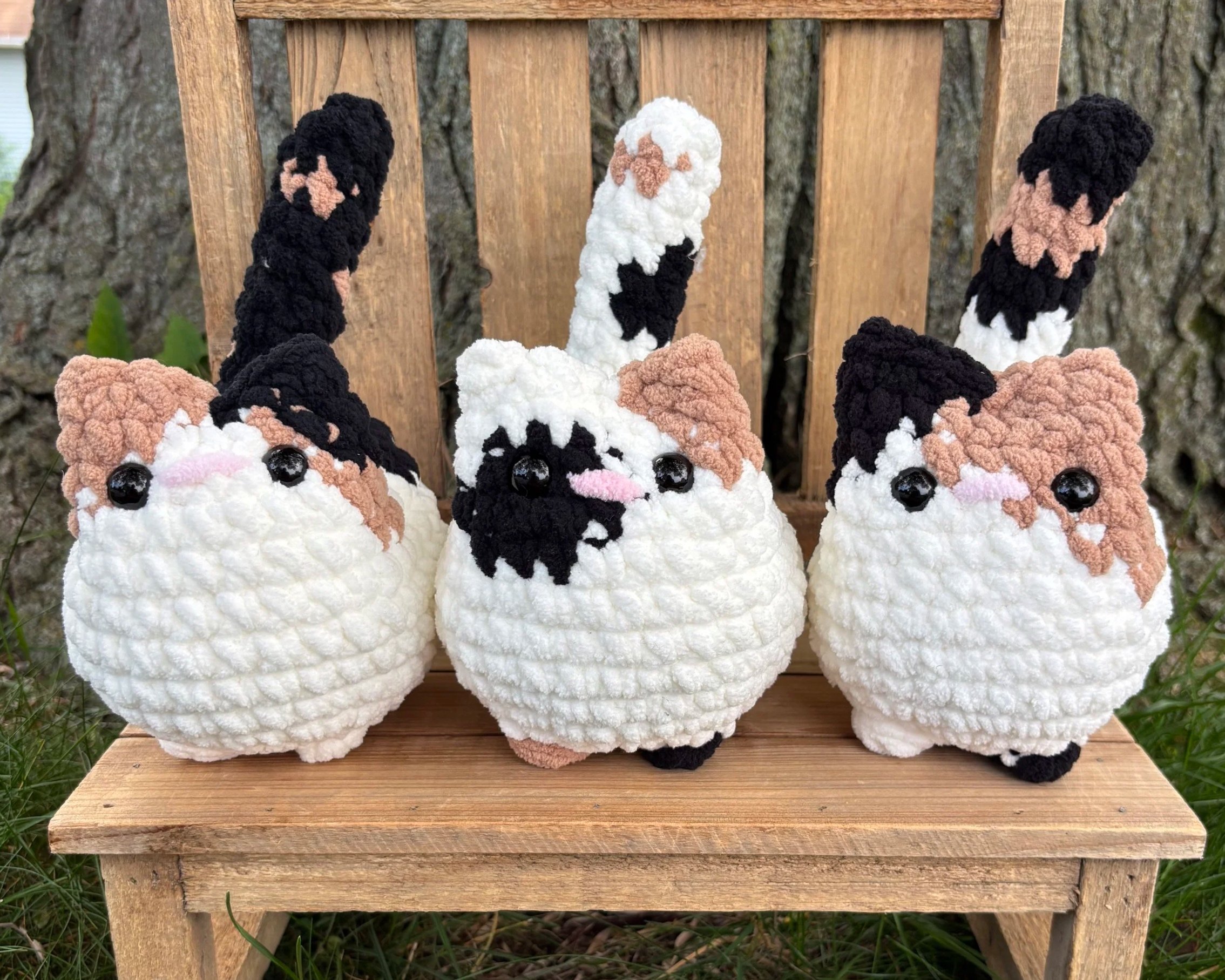 Three crochet calico cat plushies with different patterns on wooden bench